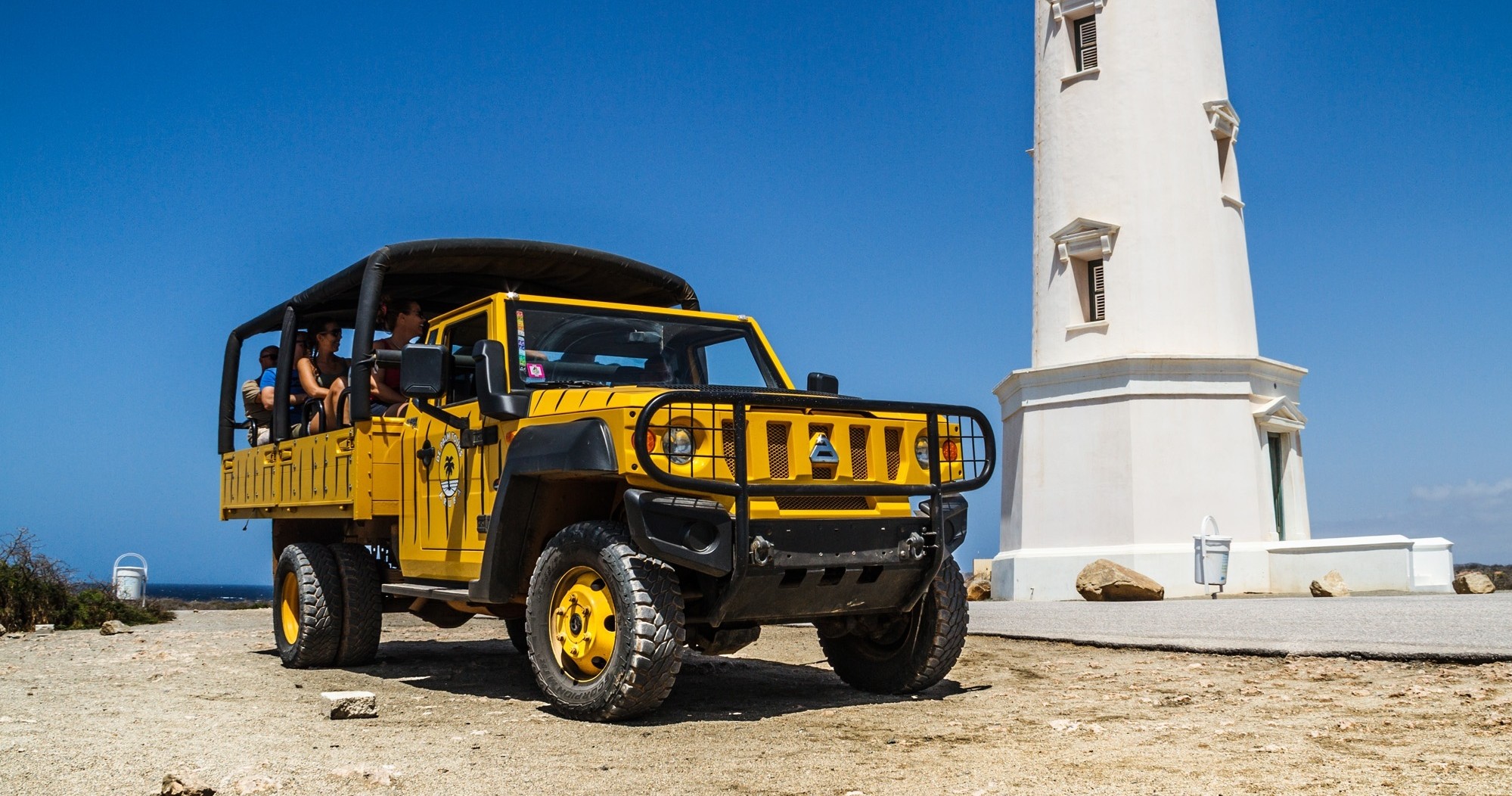 Yellow off-road vehicle near white lighthouse with blue sky.