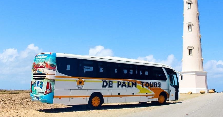 Tour bus parked near a white lighthouse on a sunny day.