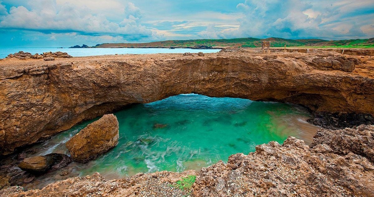 Natural rock arch over turquoise water with cloudy sky.