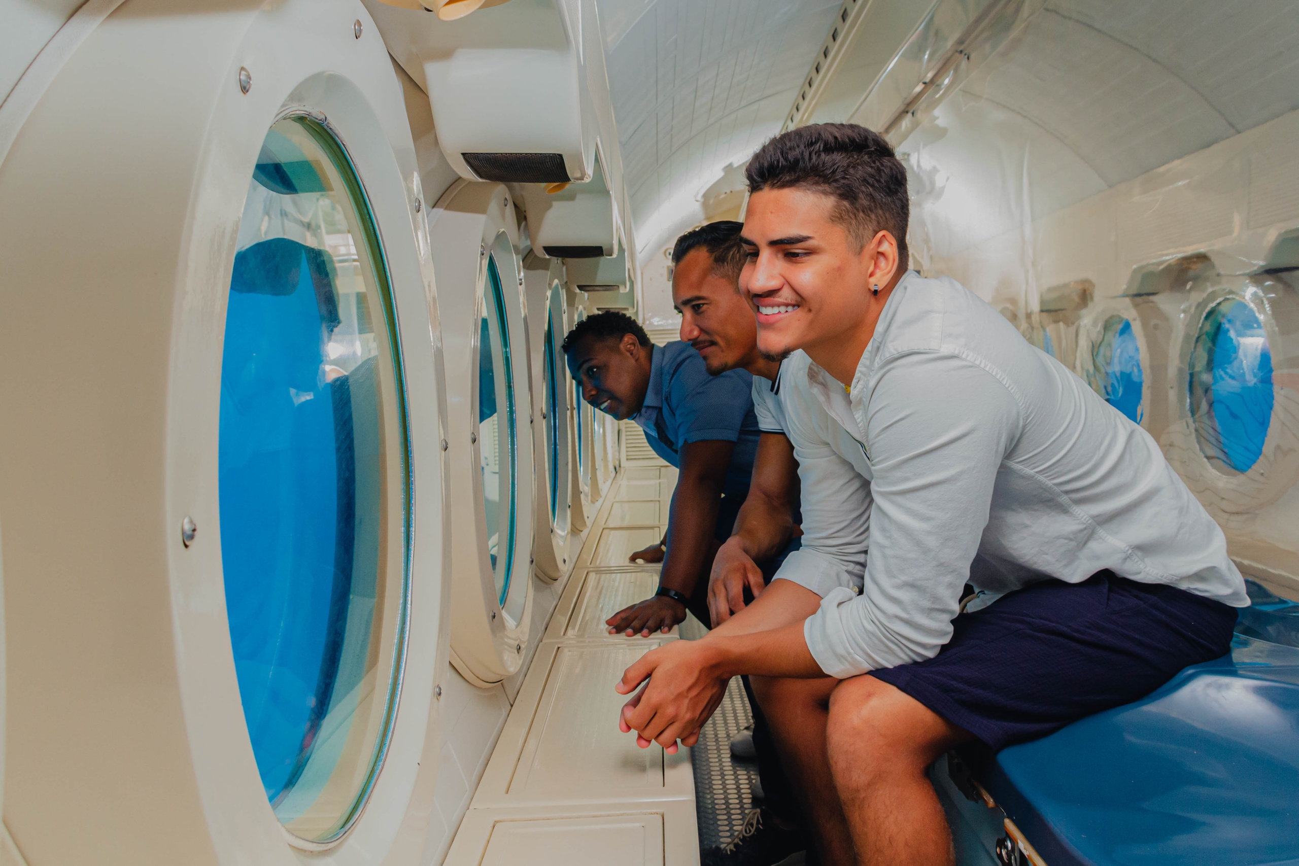 Three men smiling and looking out windows inside a submarine.
