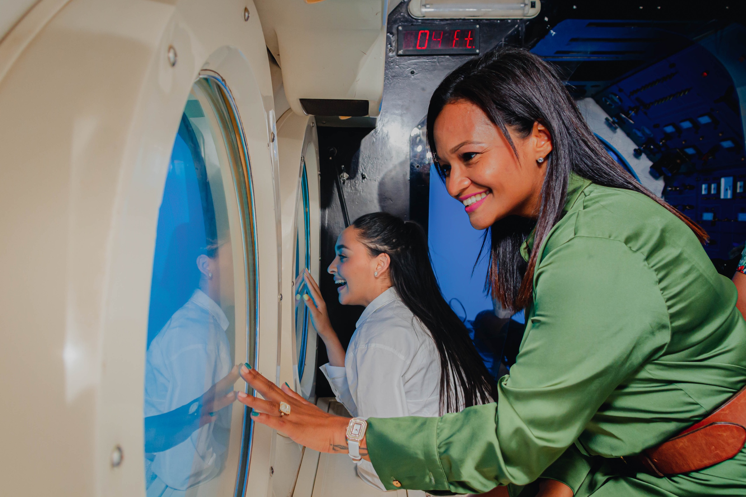 Two women smiling while looking out of submarine portholes.