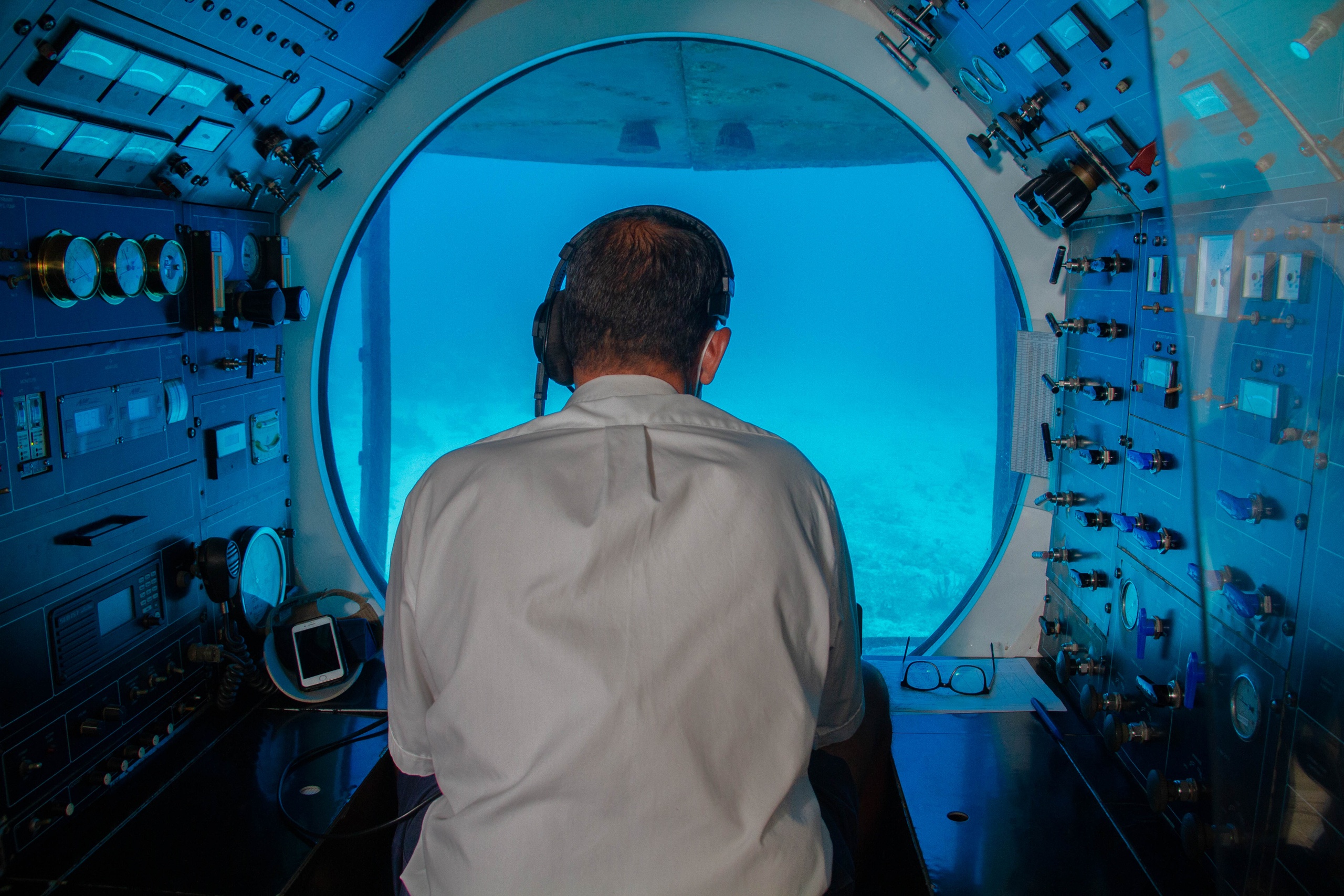 Person in a control room of a submarine, looking out a large round window at the ocean.