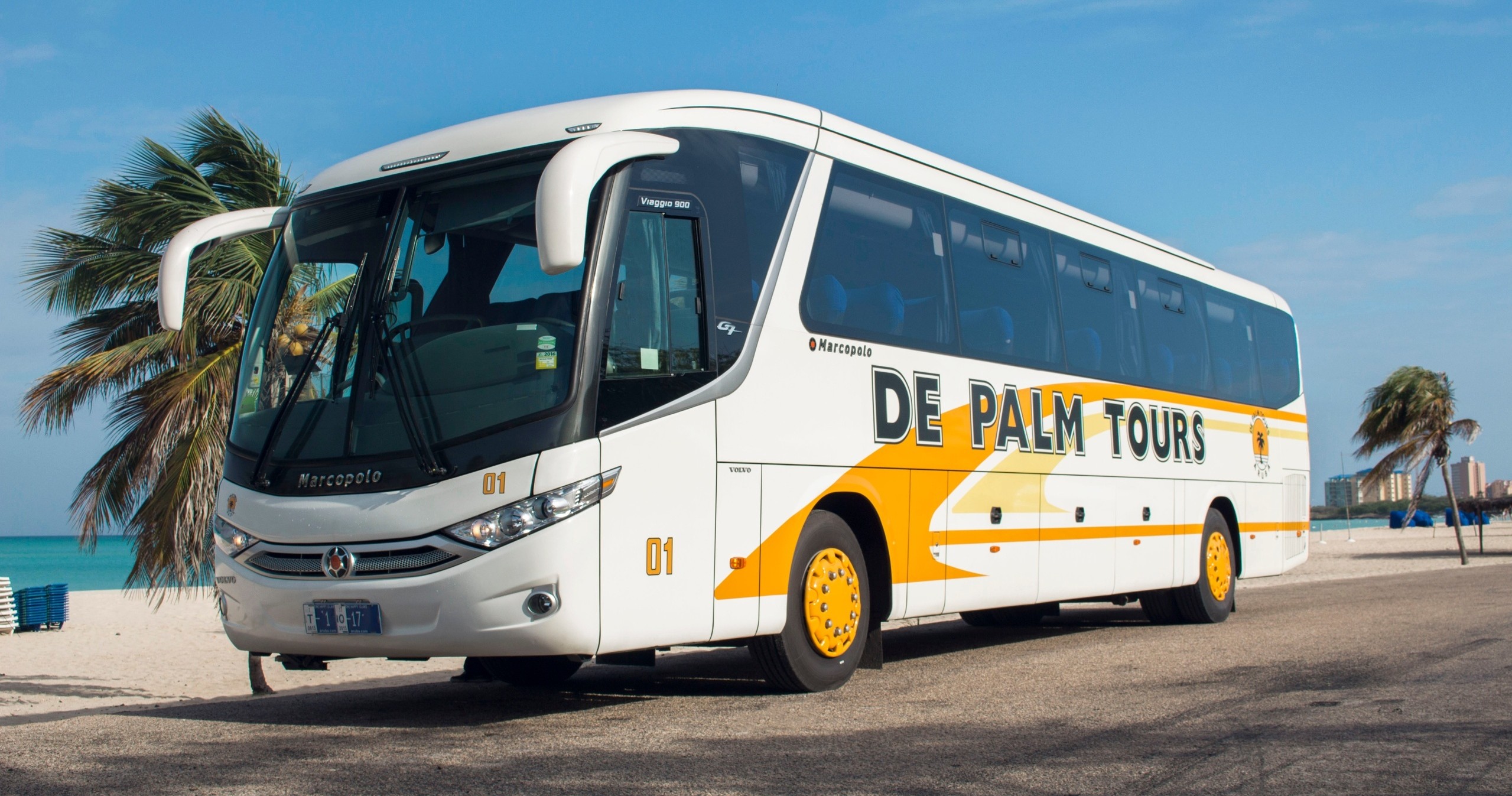 Large white and yellow tour bus parked by a beach with palm trees.