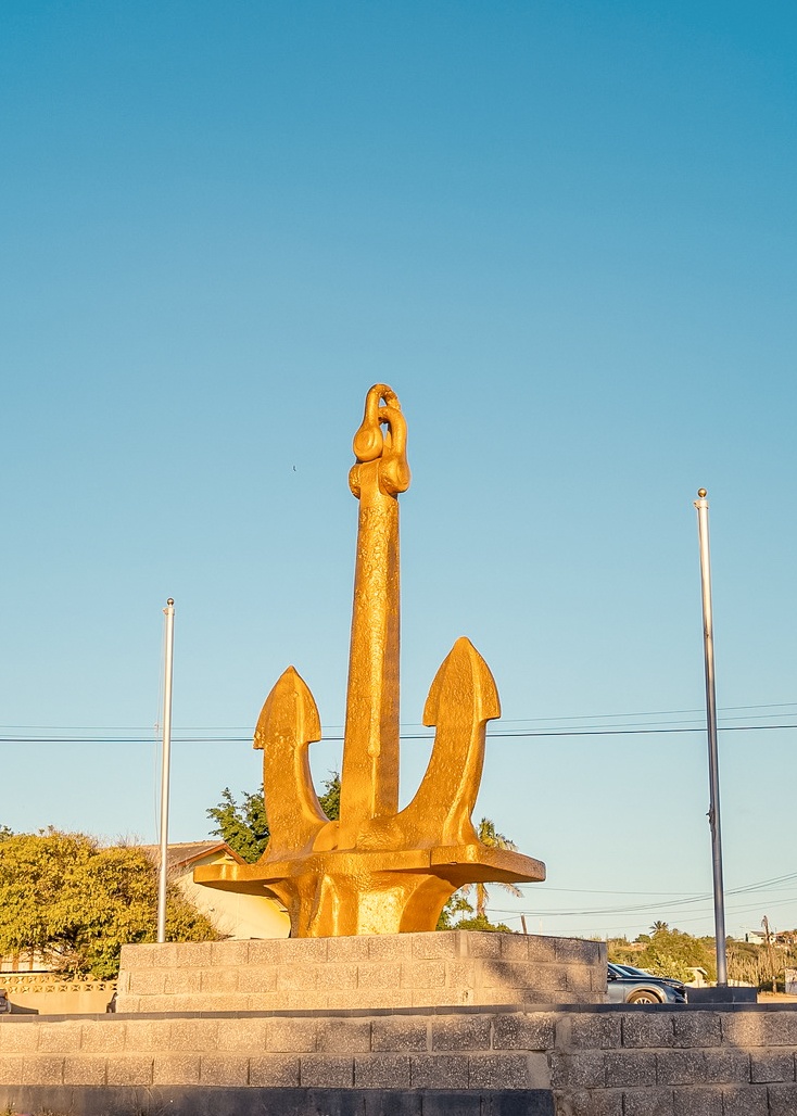 Large golden anchor statue in an outdoor setting under a clear blue sky.