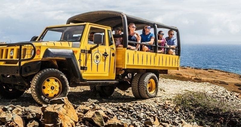 Yellow safari truck with passengers on rocky terrain near the ocean.