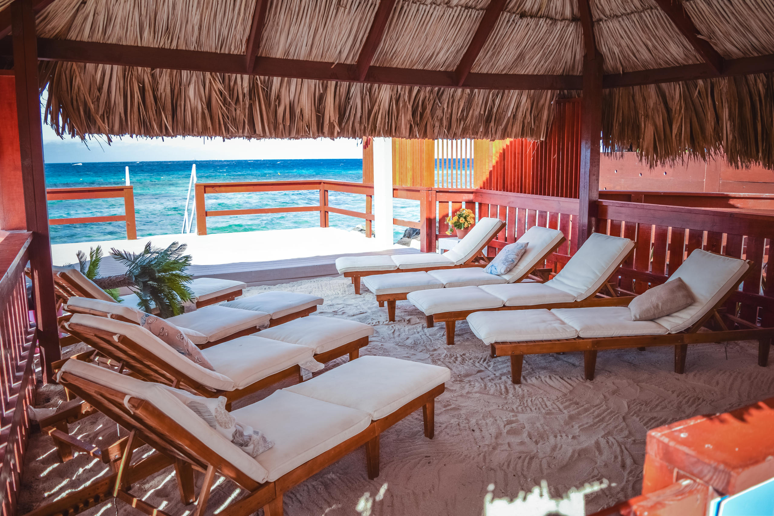Beach cabana with straw roof, sun loungers, and ocean view.