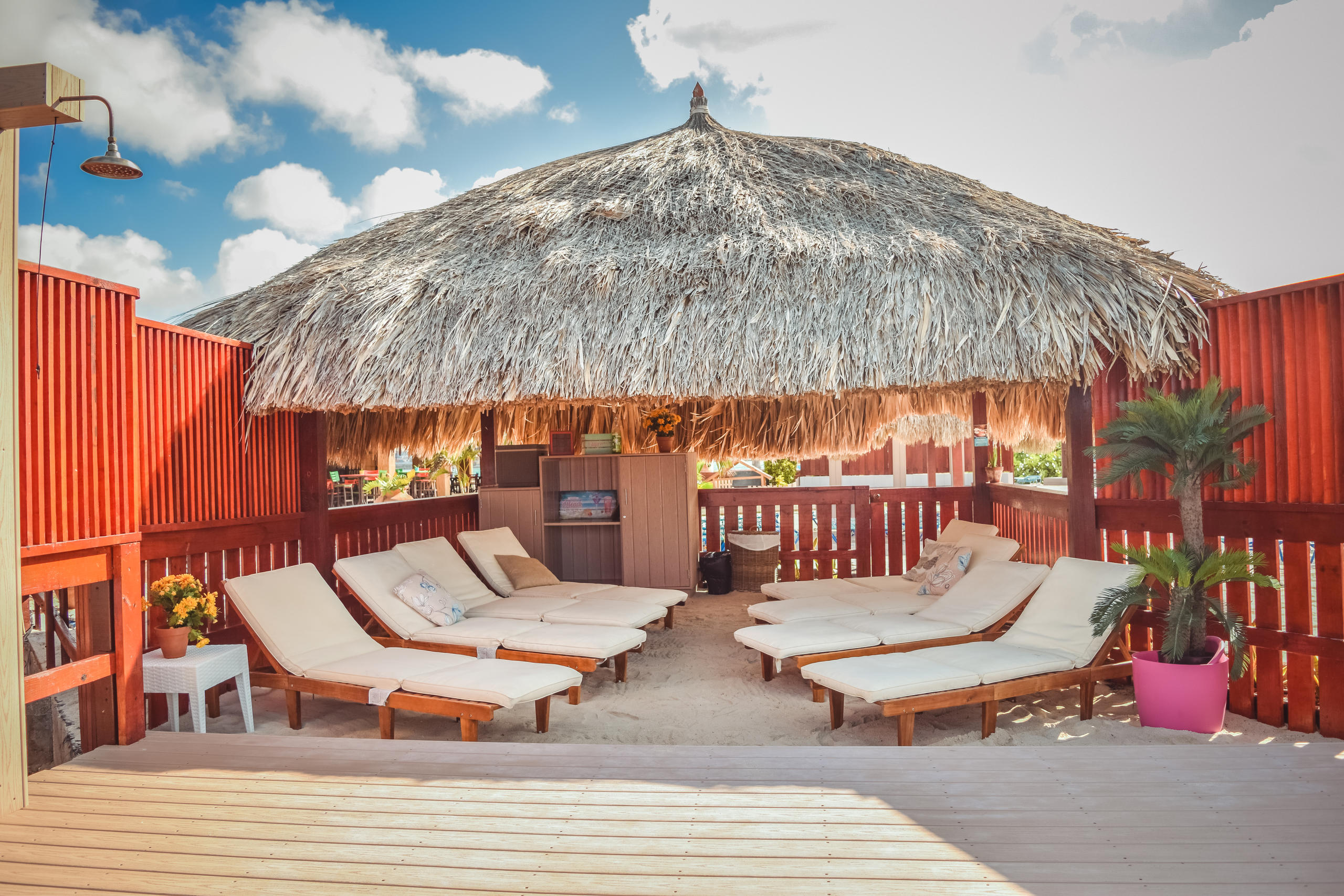 Tiki hut with lounge chairs on a wooden deck under blue sky.