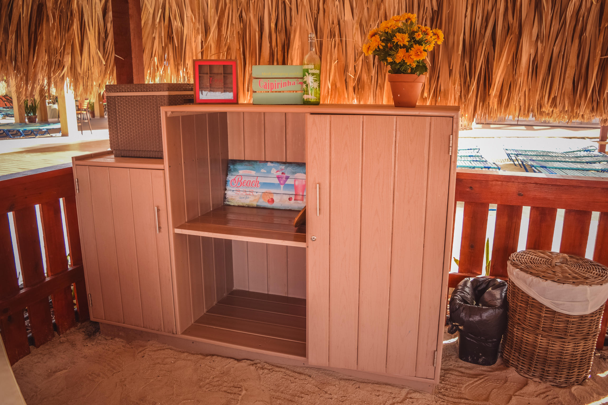 Wooden cabinet in a thatched outdoor area with decor and potted flowers.