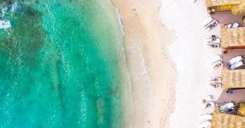 Aerial view of a beach with turquoise water and people on white sand near sunshades.