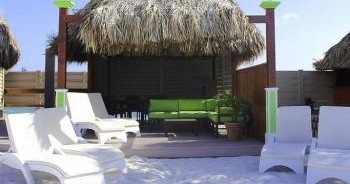 Beach cabana with lounge chairs and straw roof, sunny day.