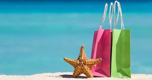 Two shopping bags and a starfish on sand by turquoise water.