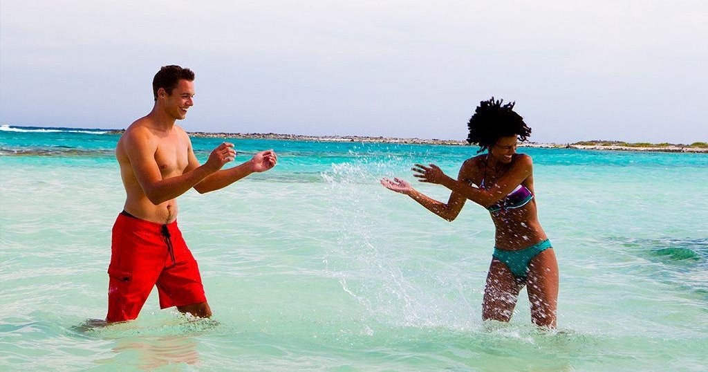 Man and woman splashing water at each other in a tropical sea.