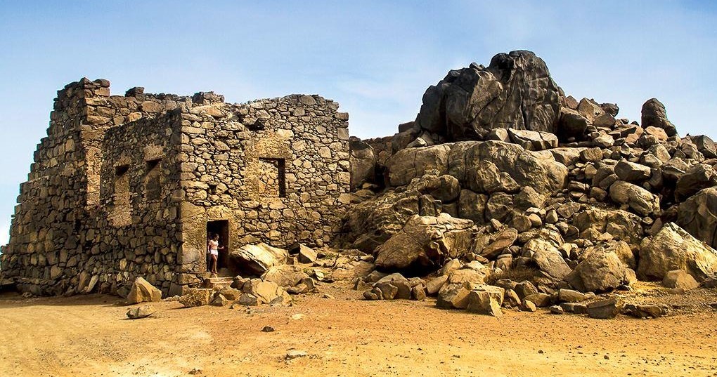 Stone ruins next to large rocky formation under a clear blue sky.