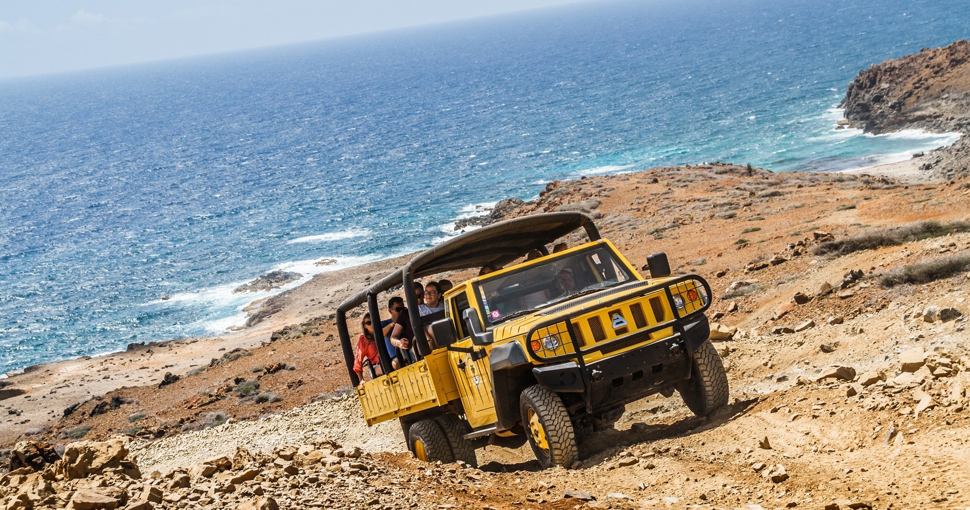 Yellow off-road vehicle on rocky terrain by the sea.