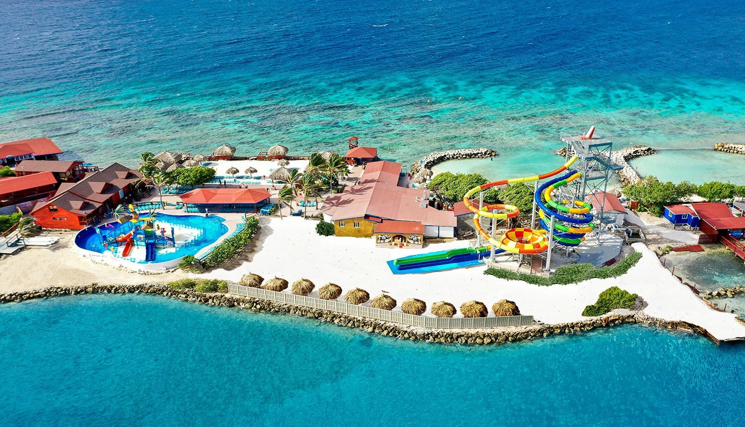 Aerial view of a tropical water park with slides and pools by the ocean.