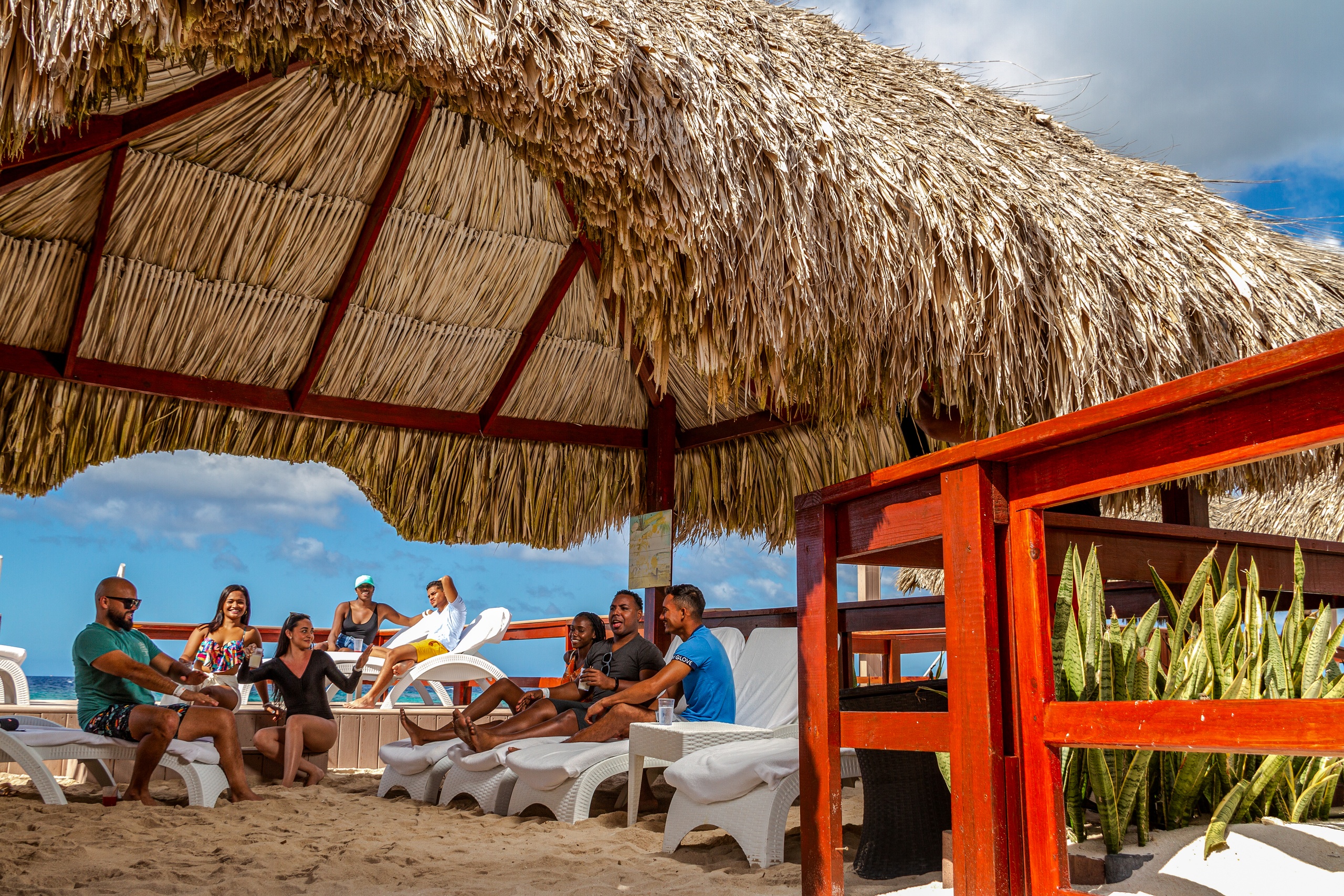 People relaxing under a thatched beach cabana on a sunny day.