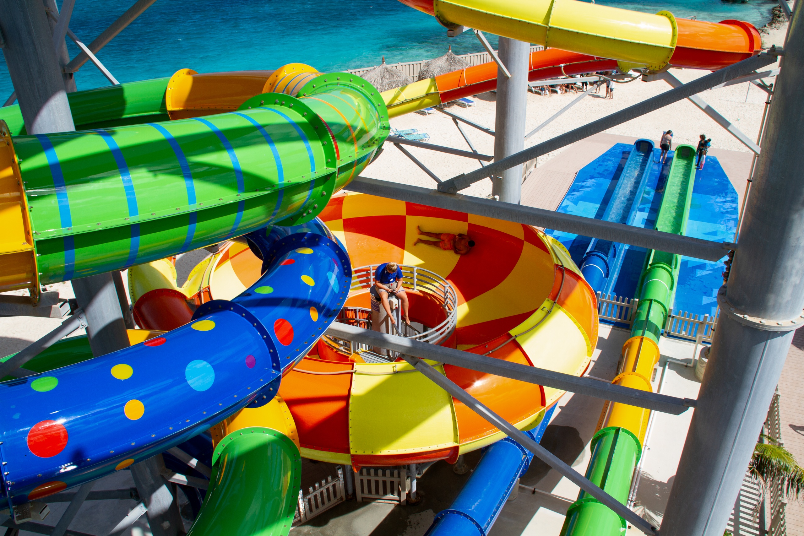 Colorful water slides twisting above a pool by a bright blue ocean.