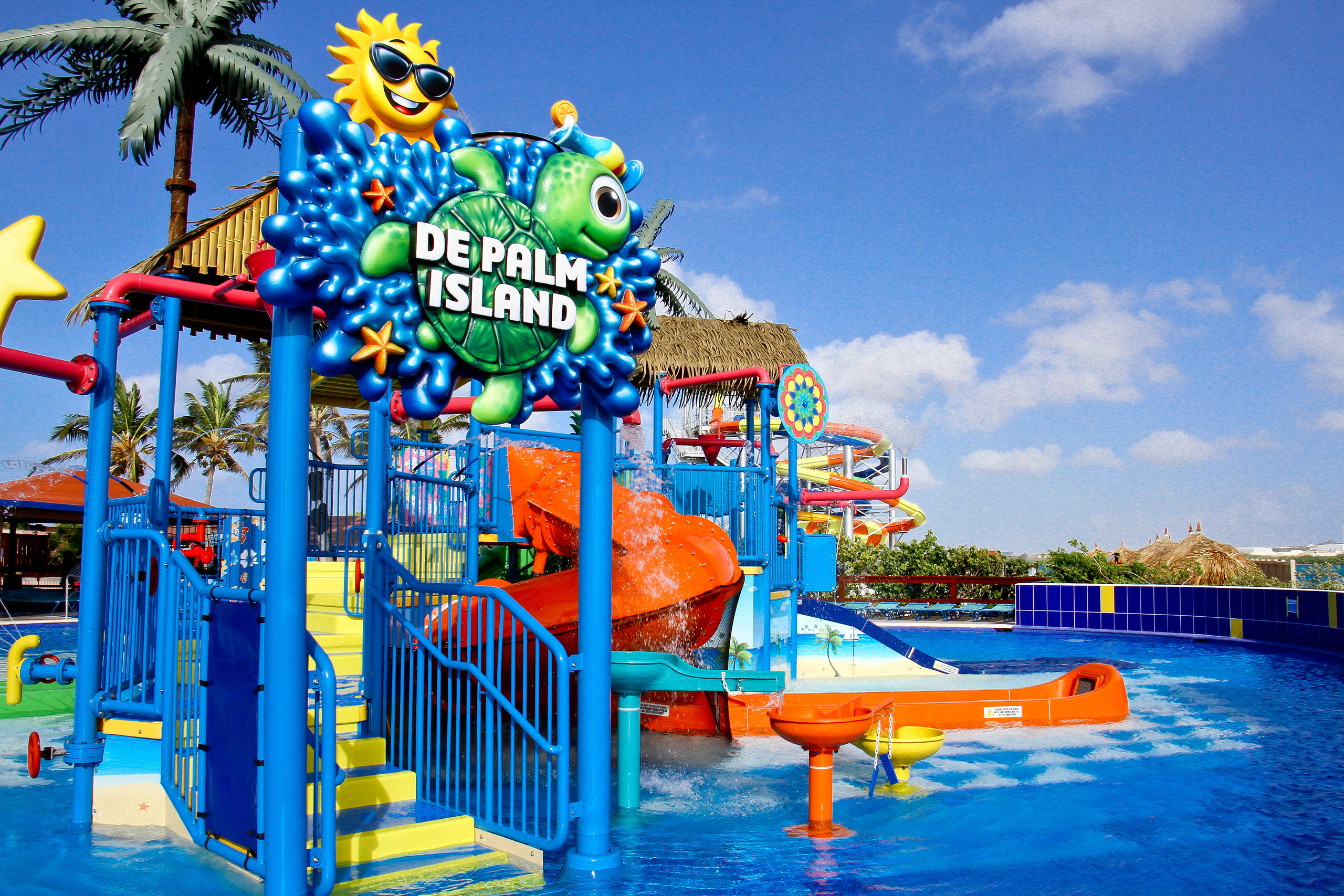Colorful water park with slides, palm trees, and 'De Palm Island' sign under a blue sky.