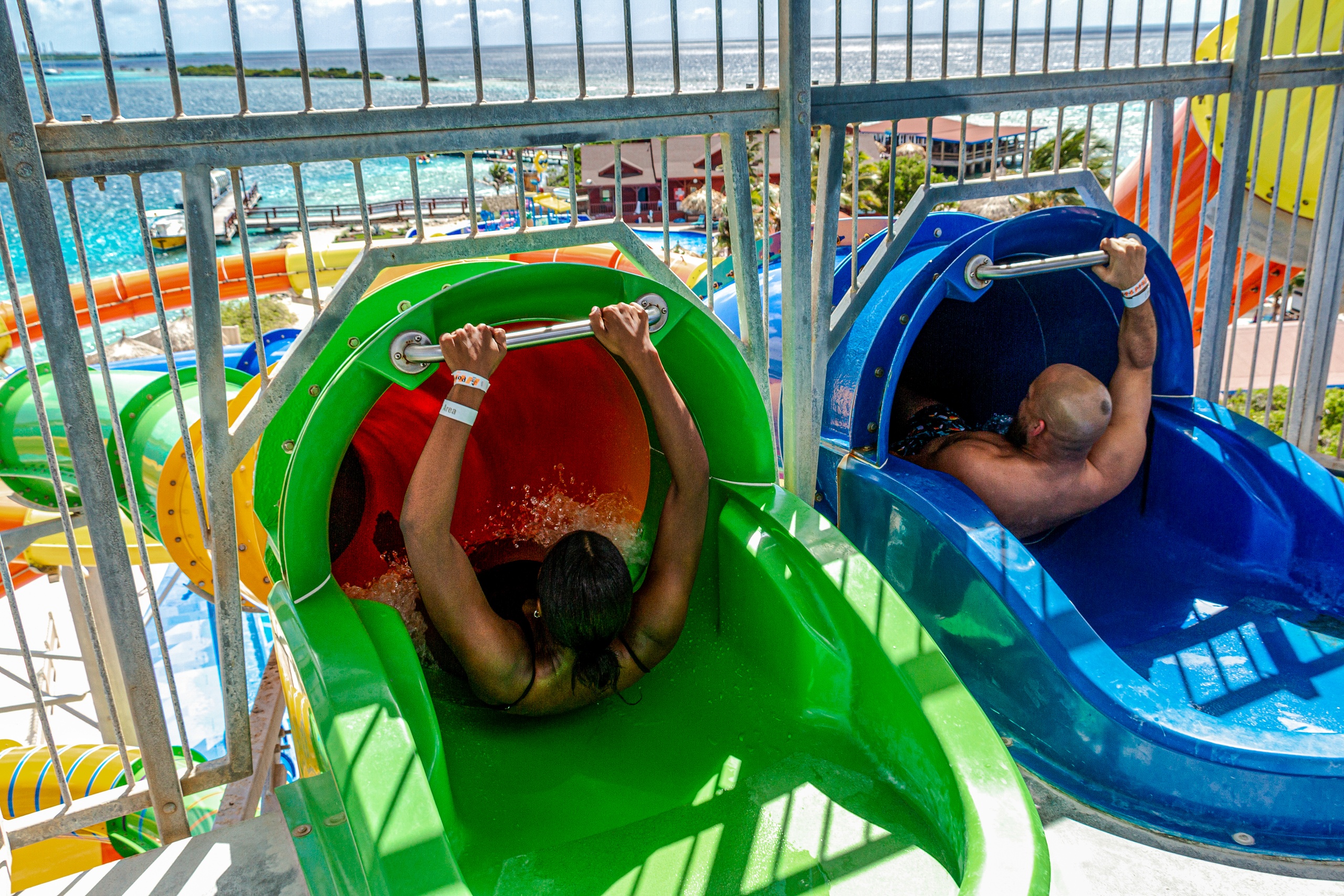 Two people hold handles before descending water slides at a water park overlooking the ocean.