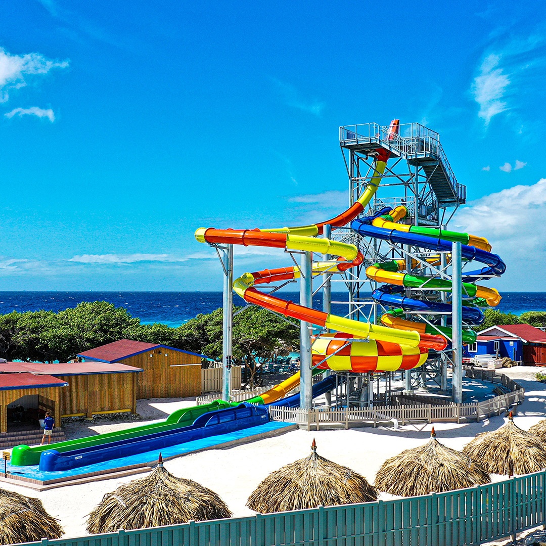 Colorful water slides and huts at a beach resort under a blue sky.
