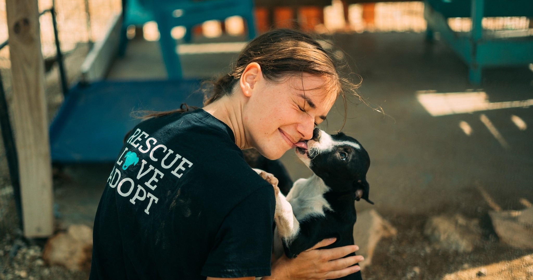 Person smiling, cuddling a black and white puppy outdoors.