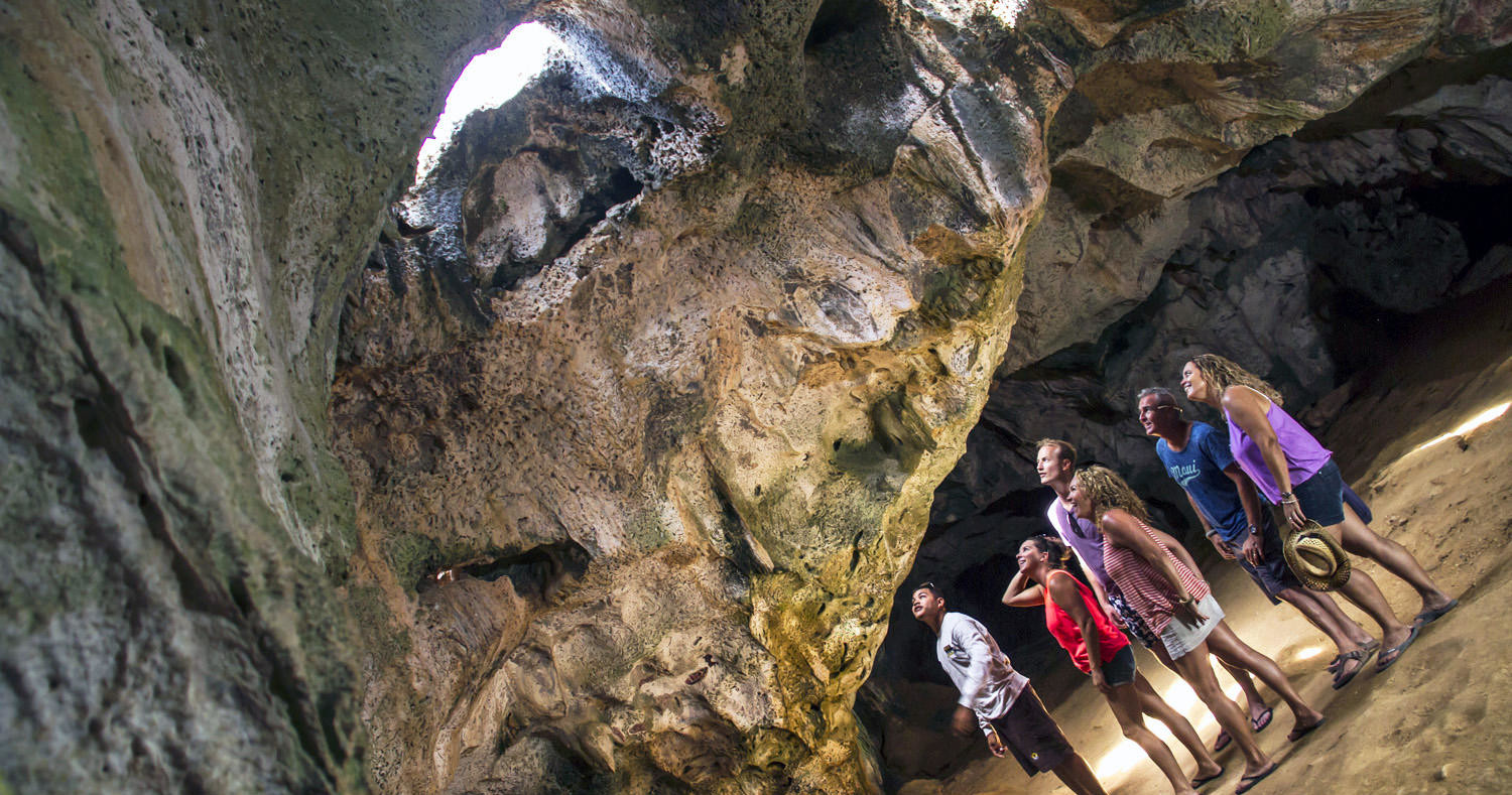 Group of people exploring a large cave with sunlight streaming in.
