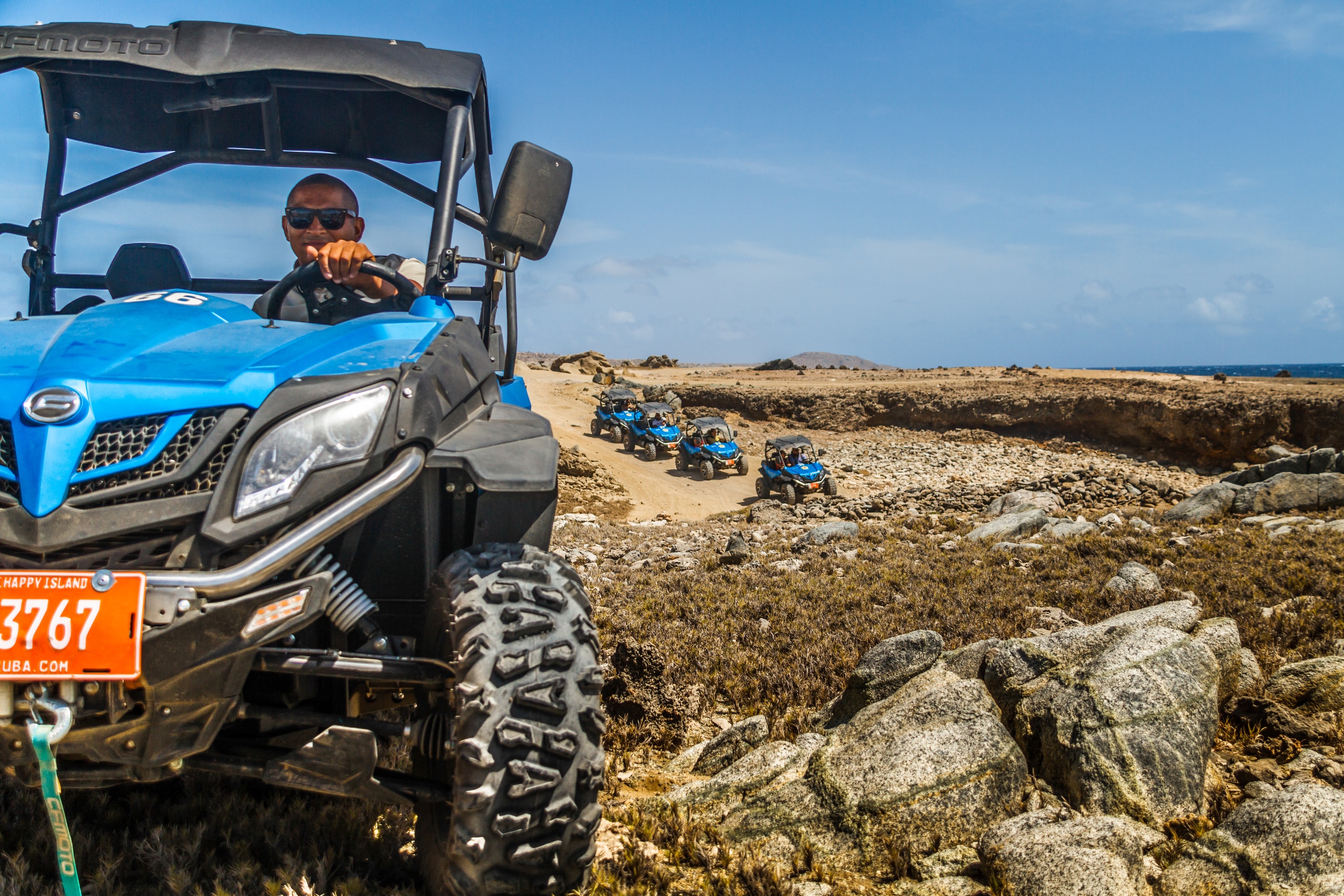 Person driving a blue off-road vehicle on a rocky path, with more vehicles in the background.