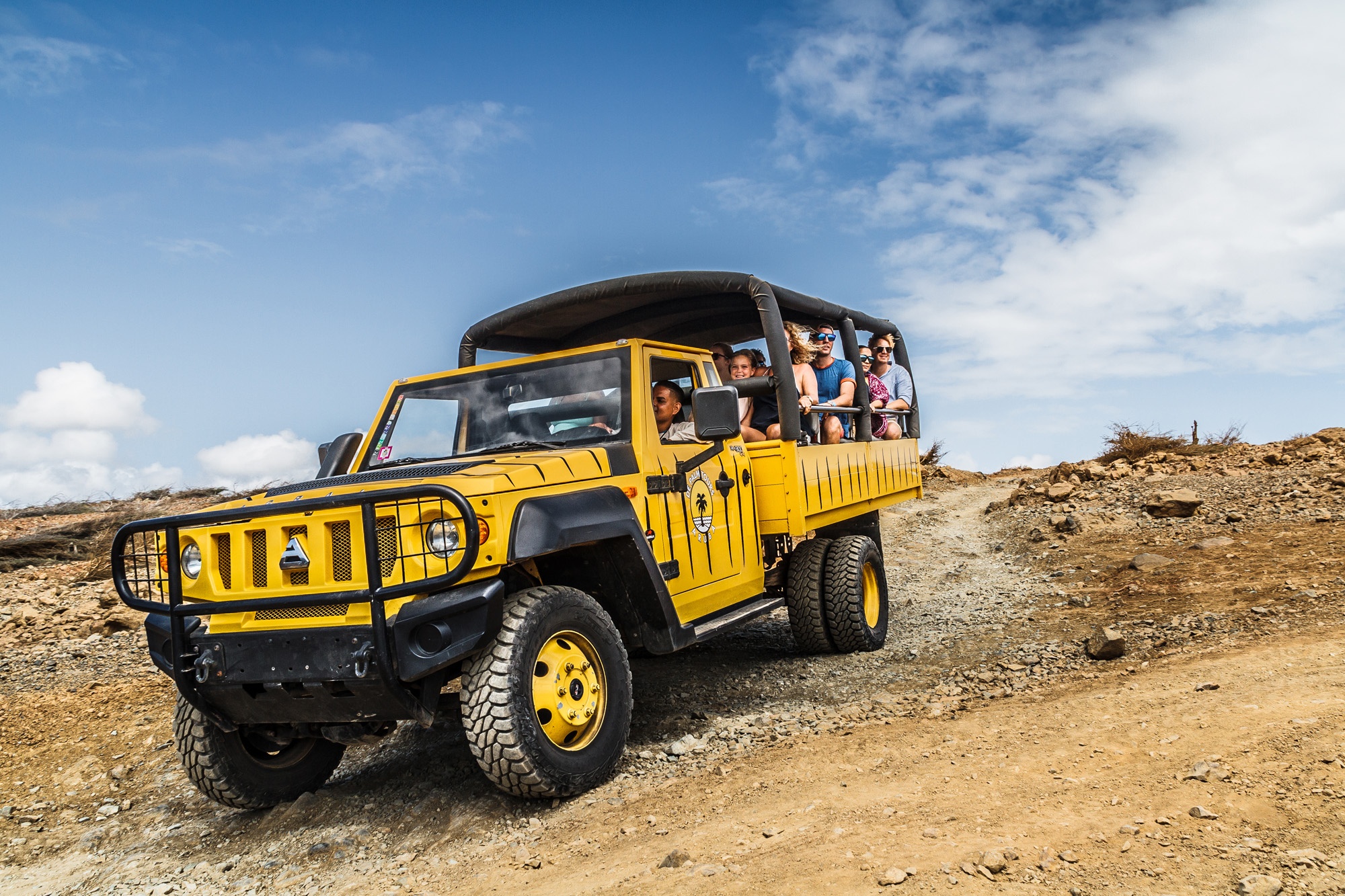 Yellow off-road vehicle on rocky terrain with passengers and blue sky.