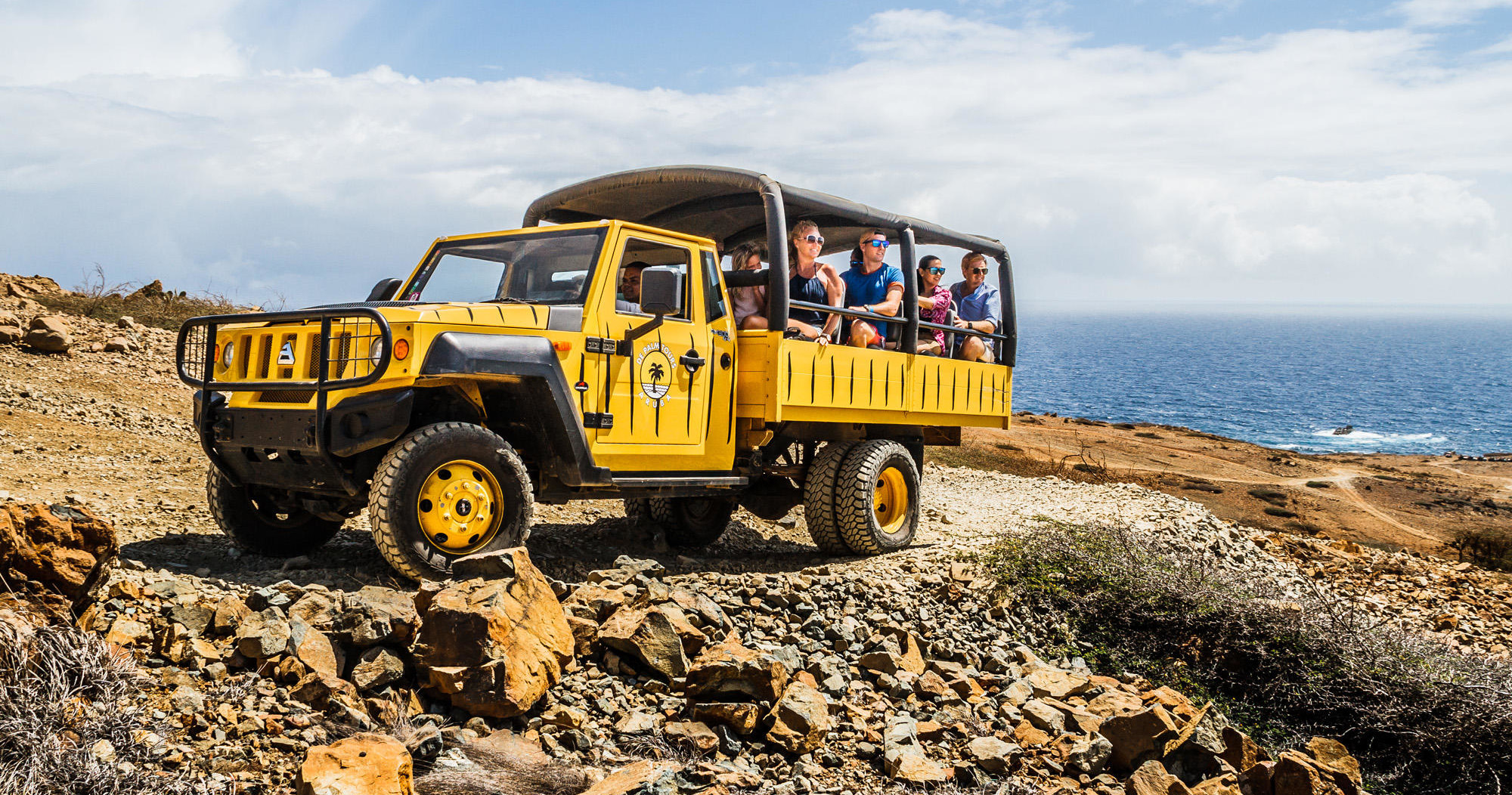Yellow safari truck with passengers on rocky coastal terrain.