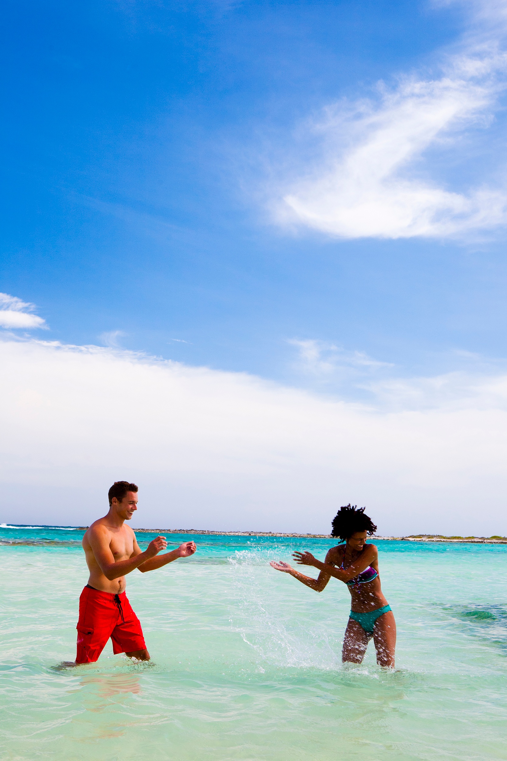 Two people playing in clear ocean water under a blue sky.