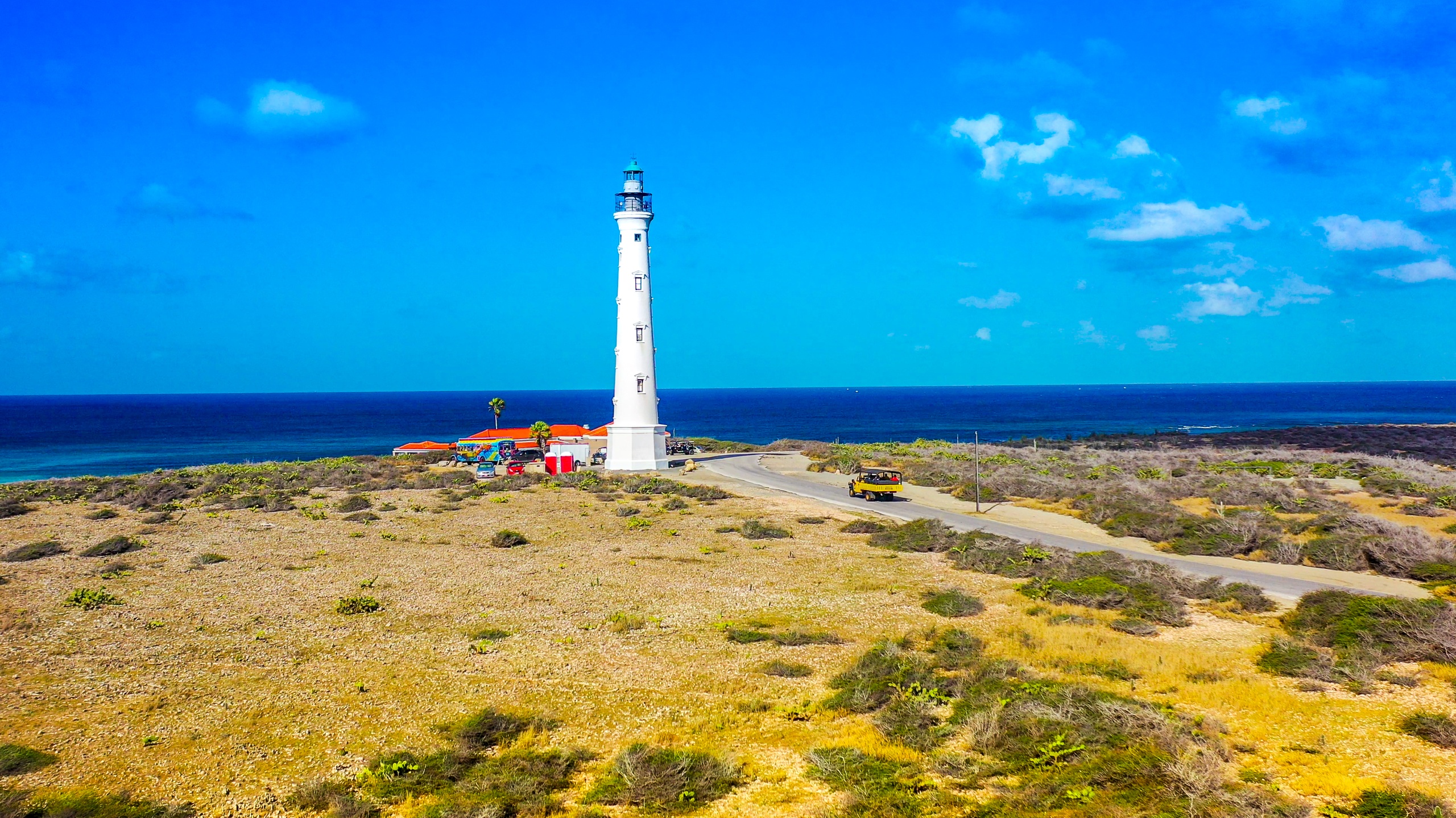Tall white lighthouse by the sea under blue sky with light clouds.