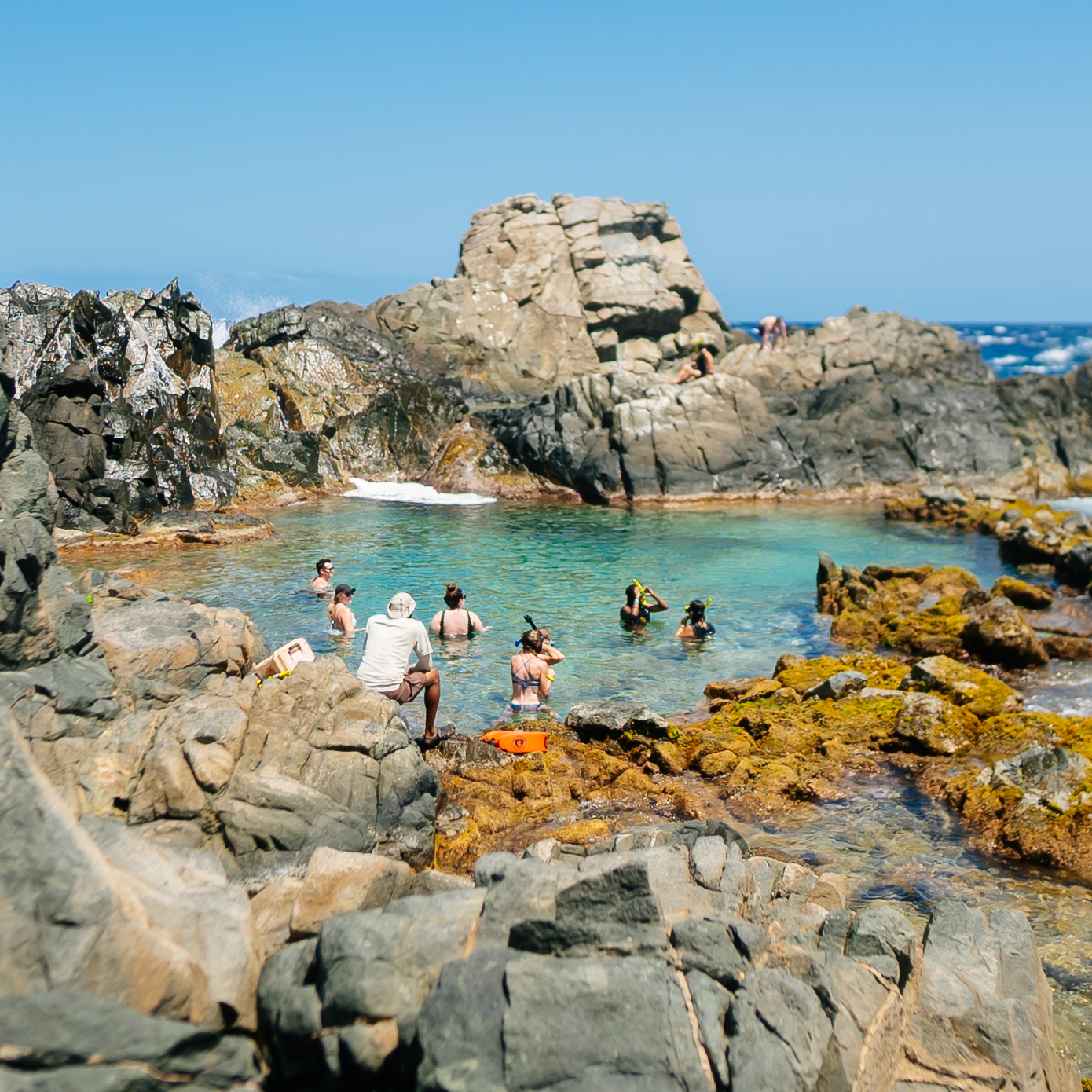 People enjoying a rocky natural pool by the ocean.