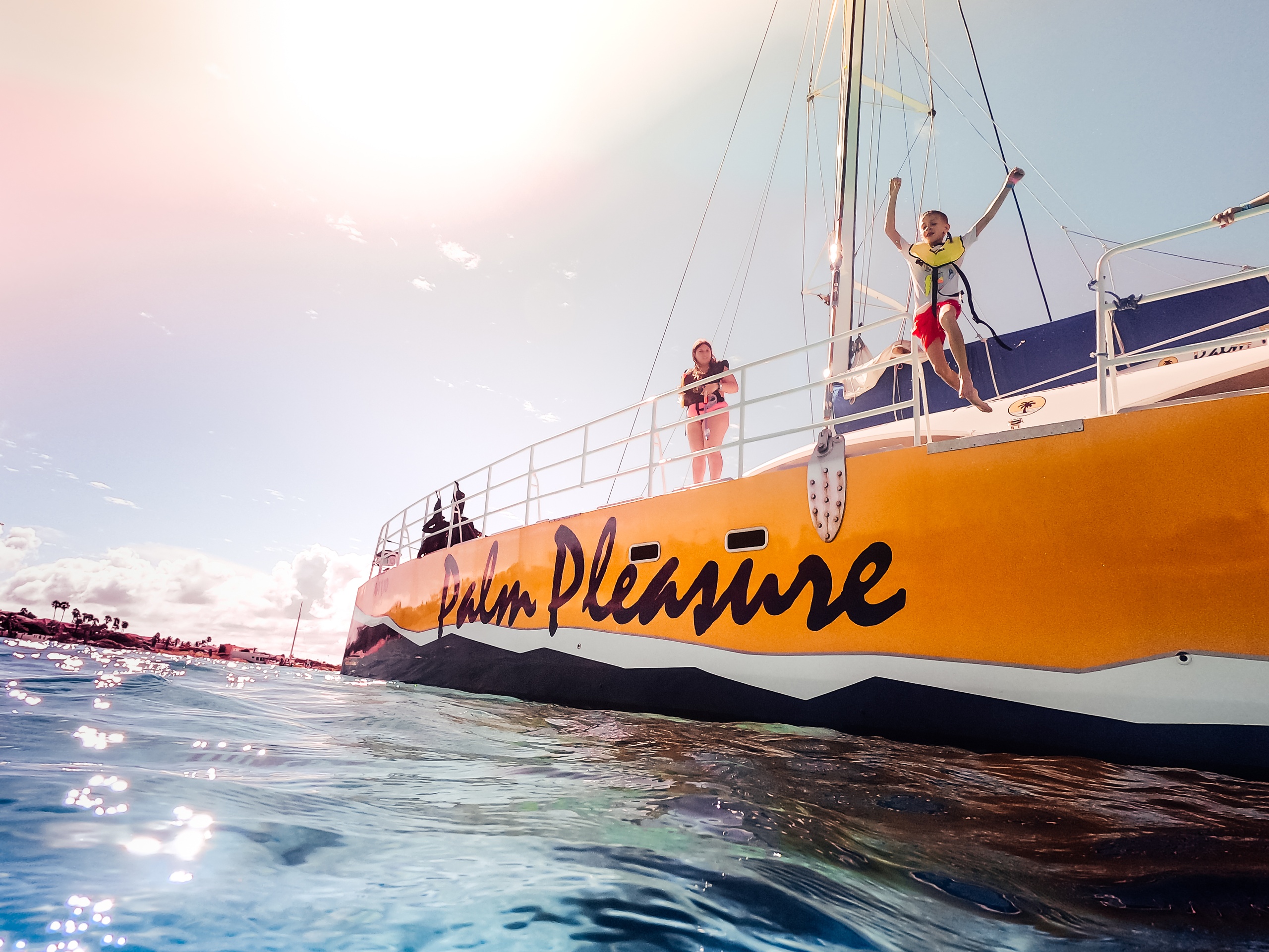 People on a boat named 'Palm Pleasure' under a bright sun, with blue sky and ocean.