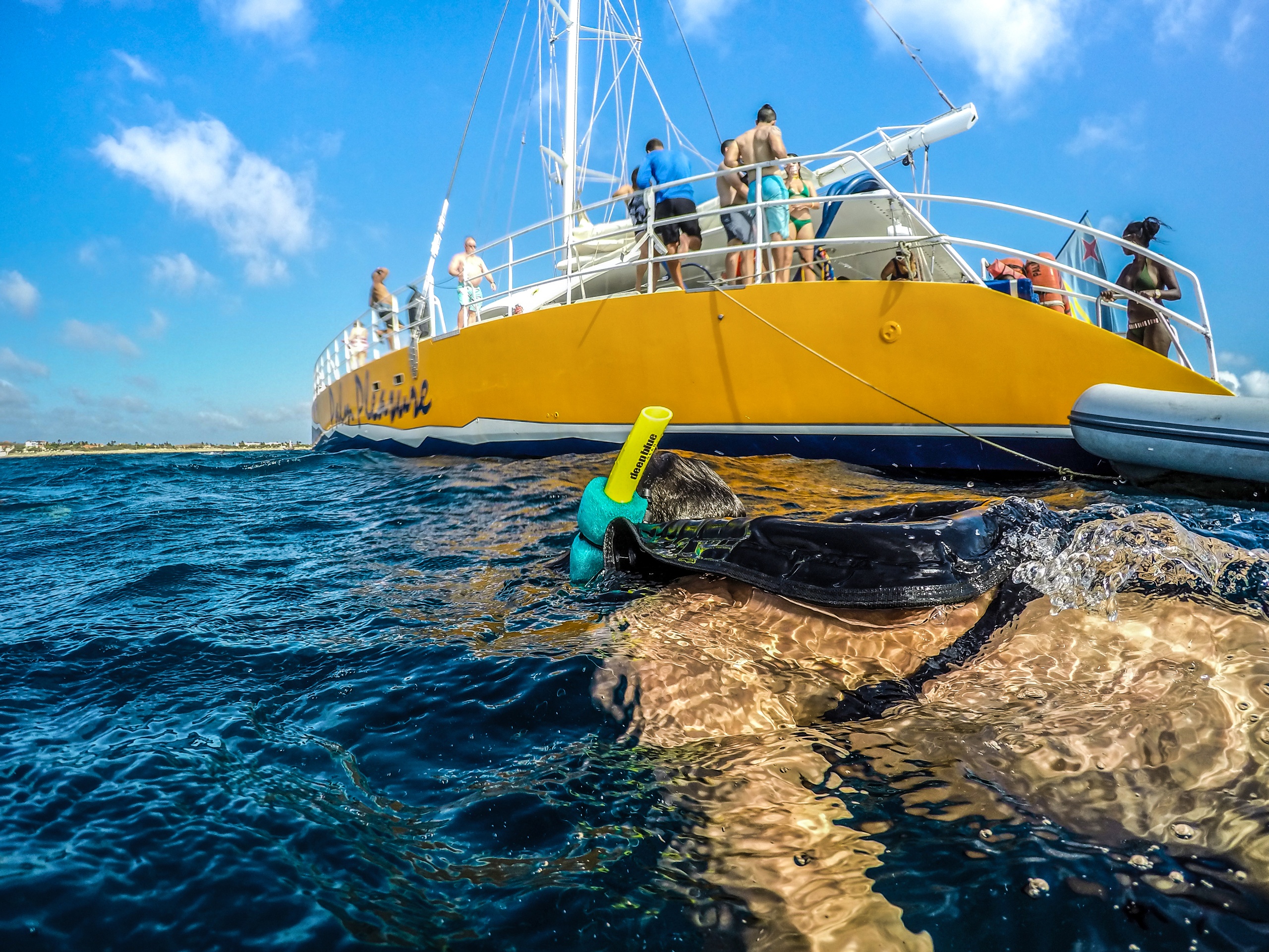Person snorkeling near a yellow boat with people onboard on a sunny day.