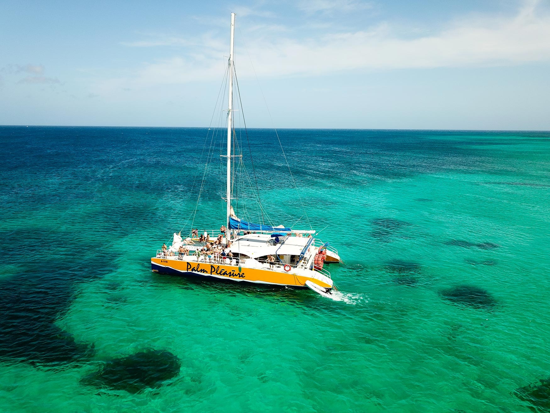Catamaran sailing on turquoise sea with clear blue sky.
