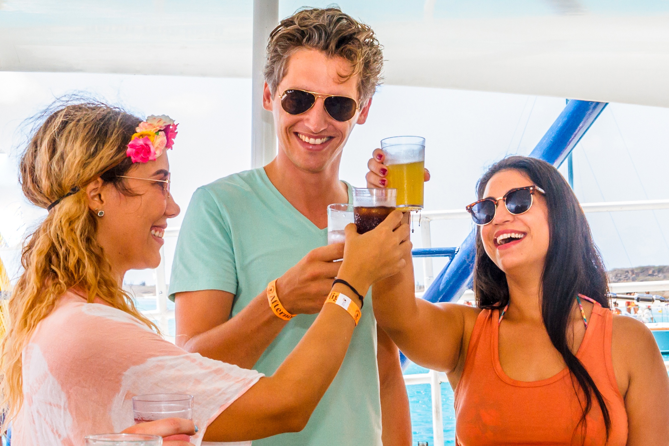Three people smiling and toasting drinks on a boat.