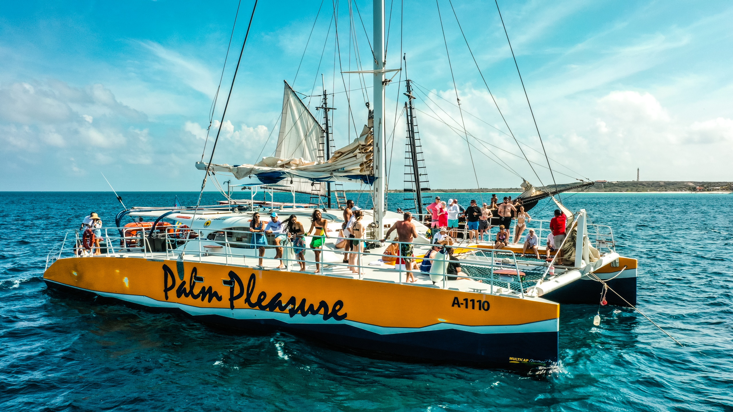 Yellow catamaran with people sailing on open water under blue skies.