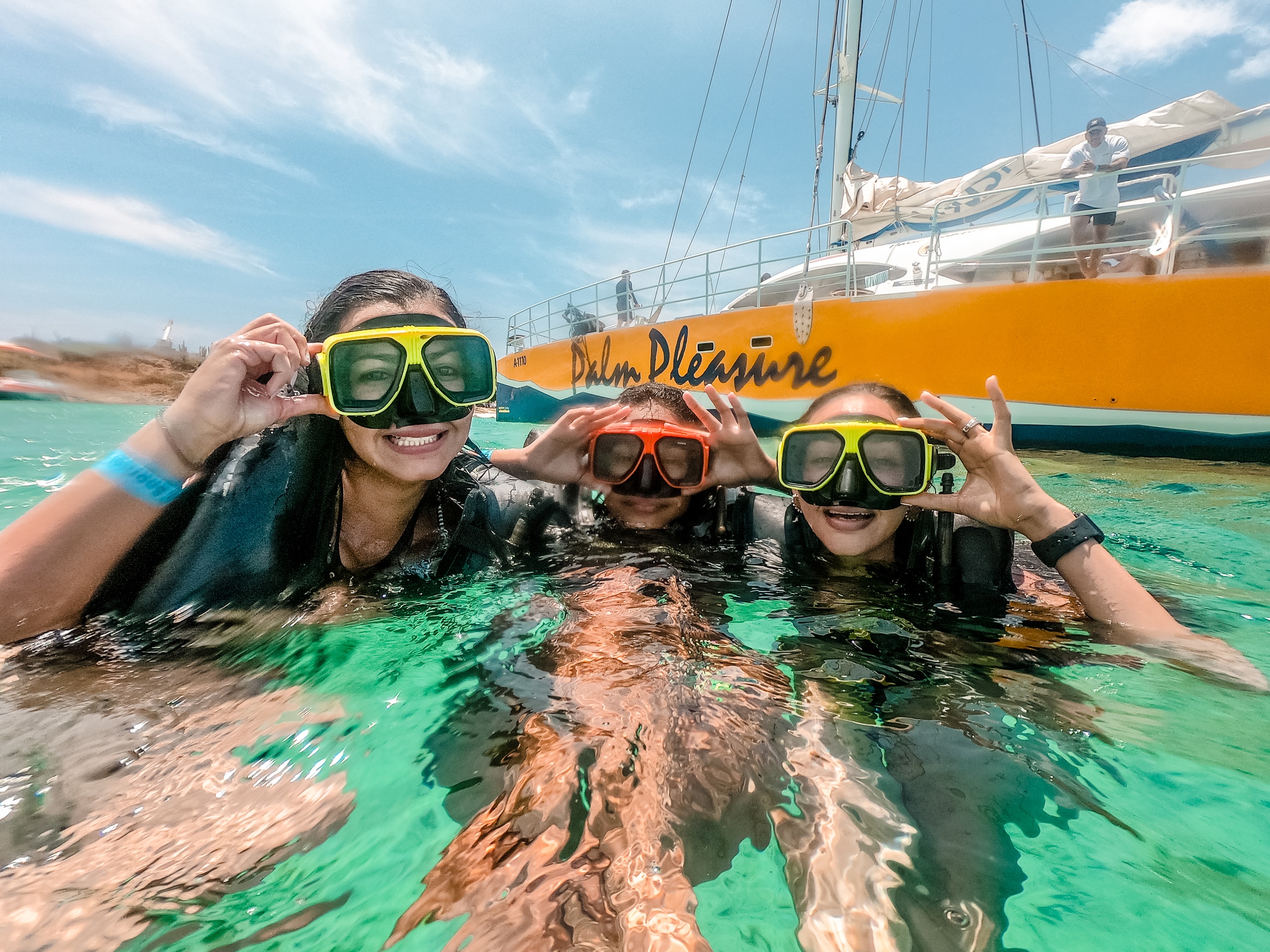 Three people in water with snorkel masks near a yellow boat.