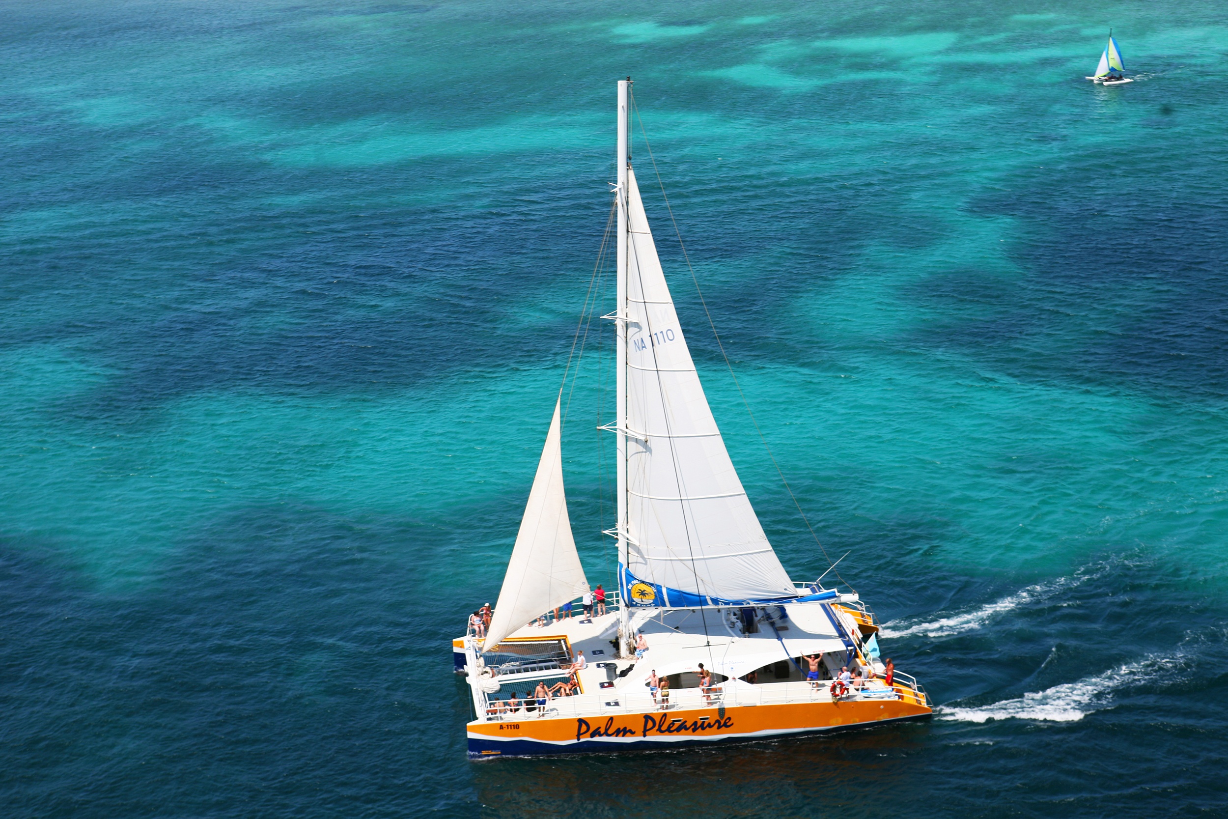 Catamaran with white sails on turquoise and dark blue ocean.