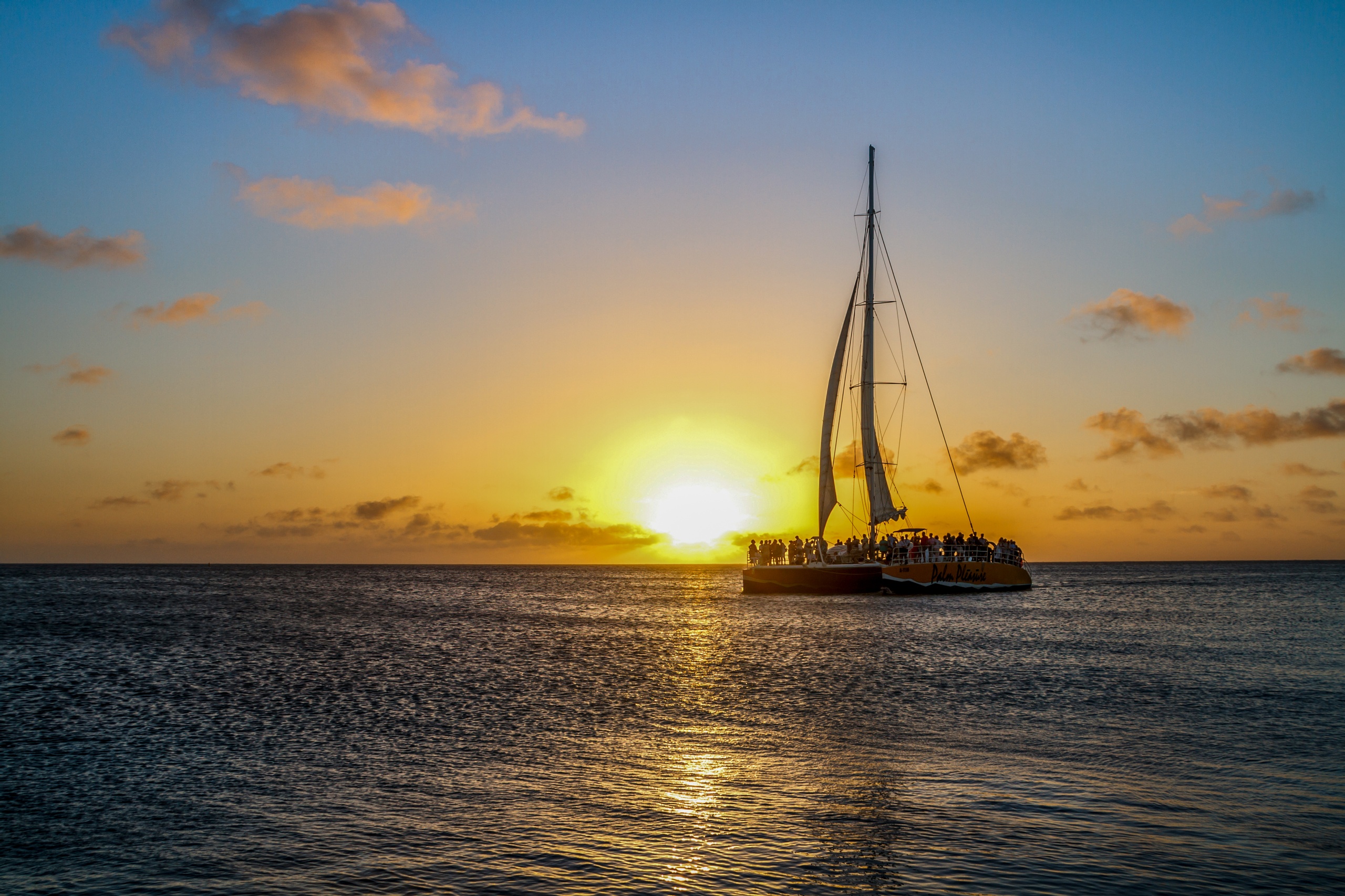 Sailboat on ocean at sunset with golden sky.