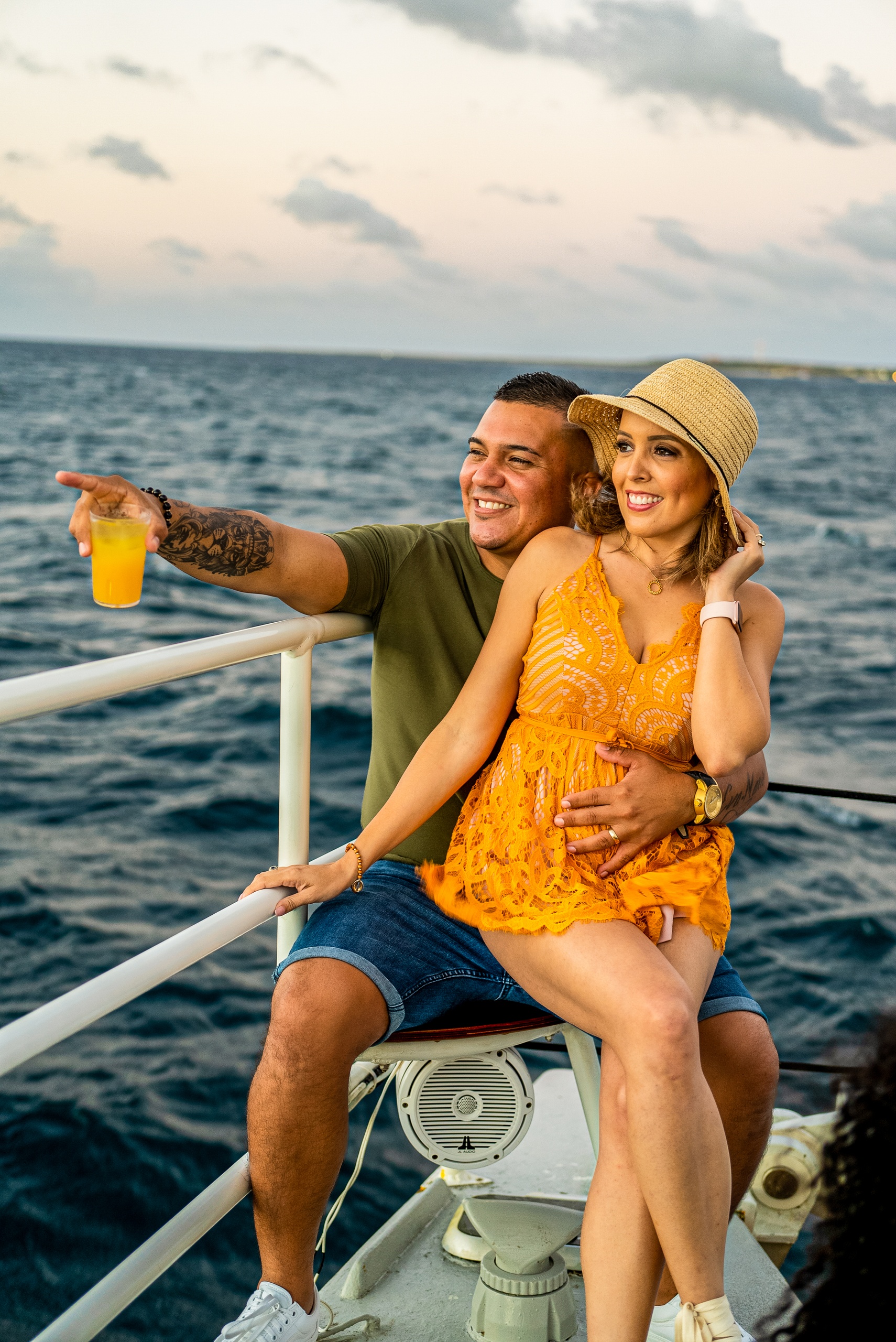 Couple on boat, woman in orange dress, man pointing, with ocean view.