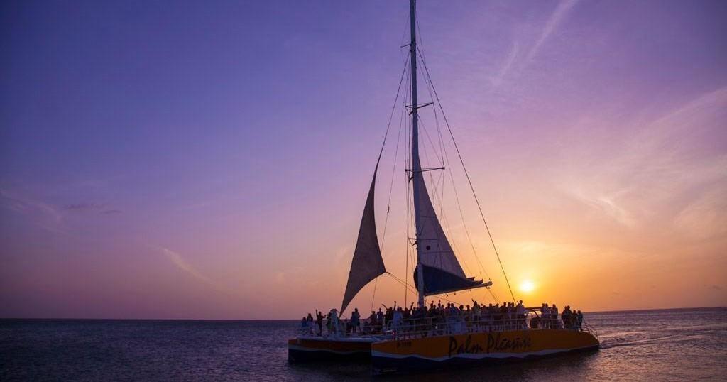 Silhouetted sailboat on ocean at sunset with passengers on deck.