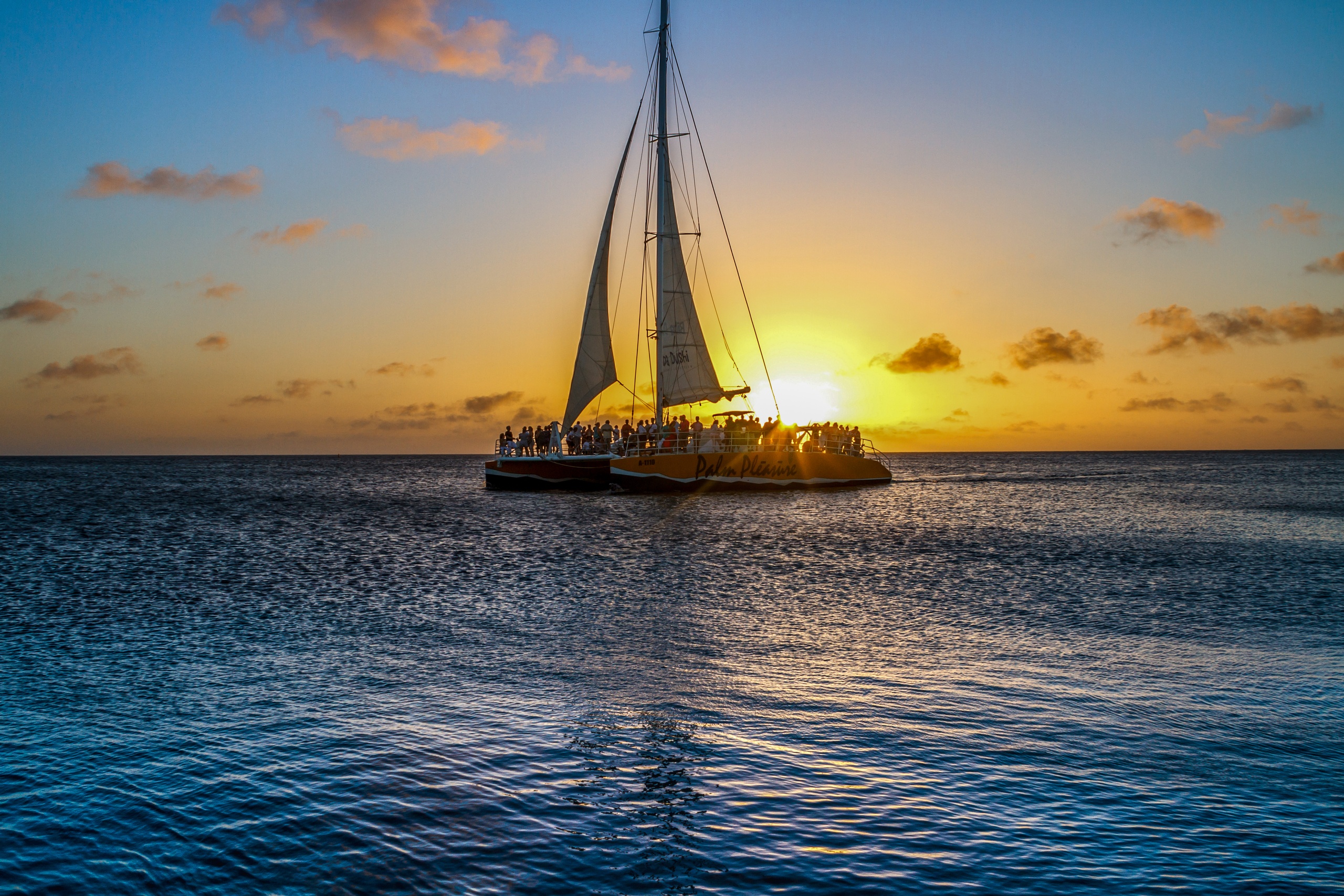 Sailboat silhouetted against a vibrant sunset over calm ocean waters.