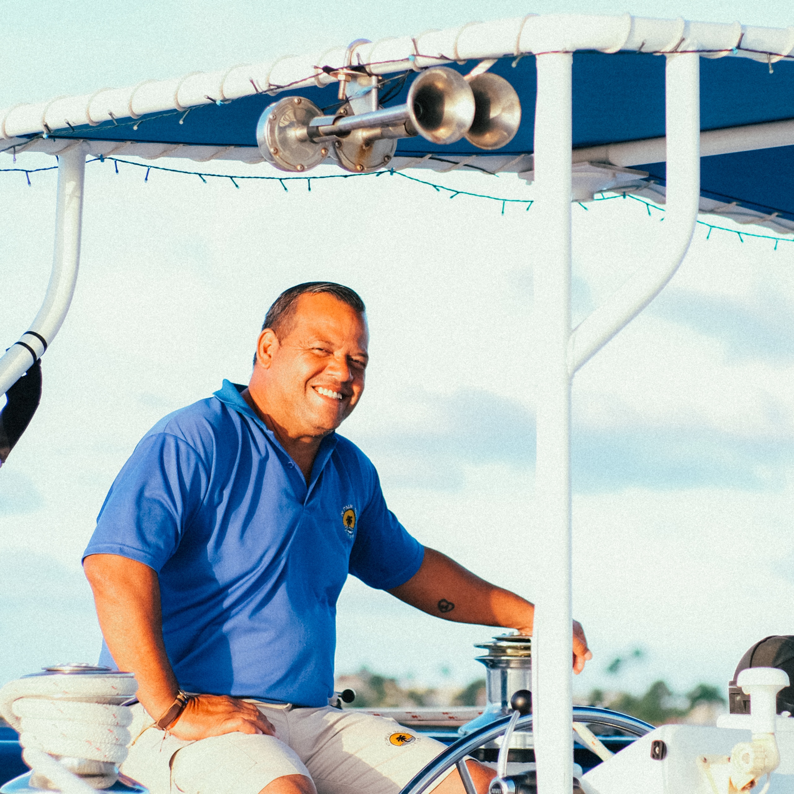 Smiling man in blue shirt steering a boat under sunny sky.