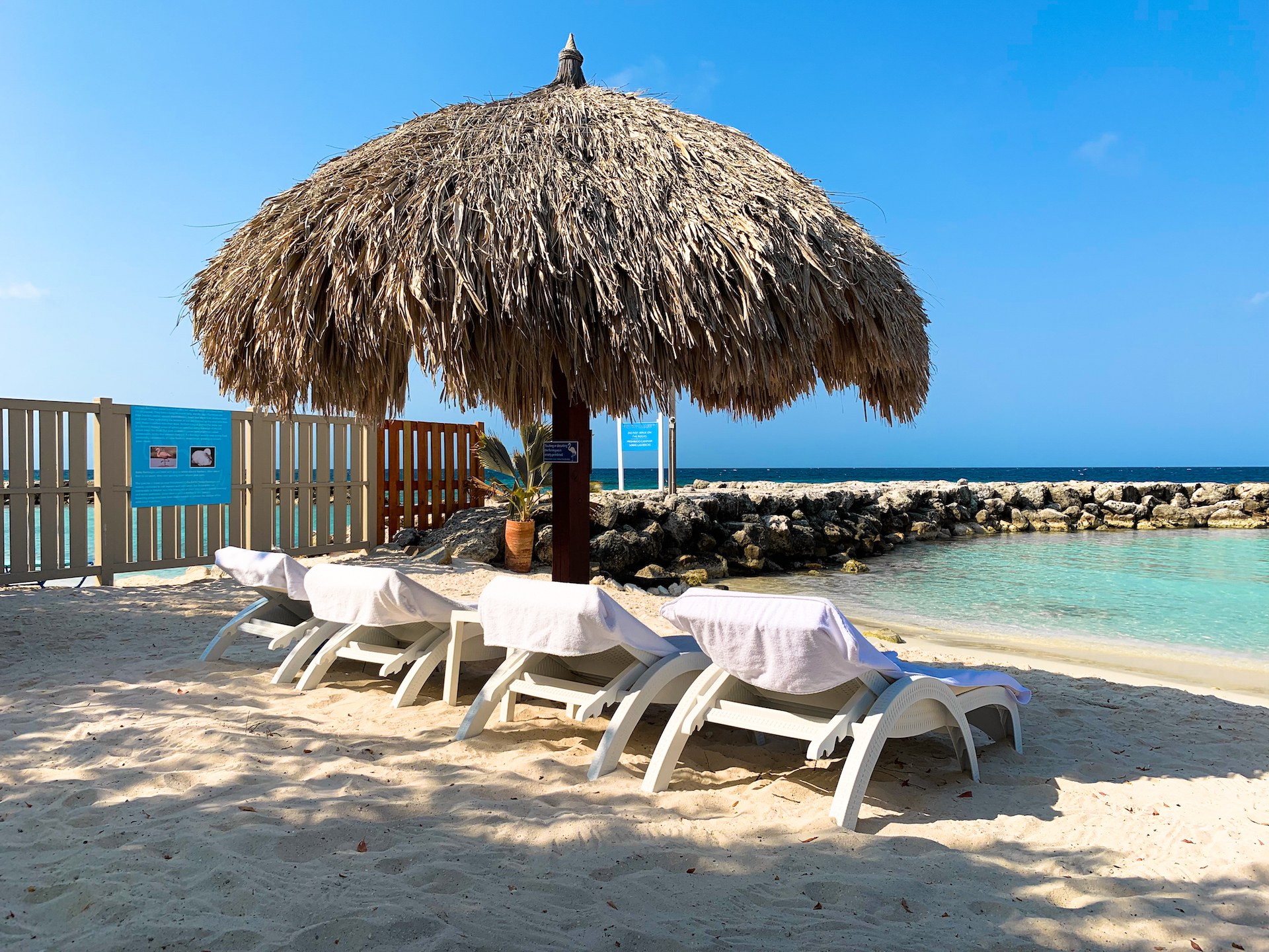 Beach with straw umbrella, four loungers, sand, and rocky shoreline.