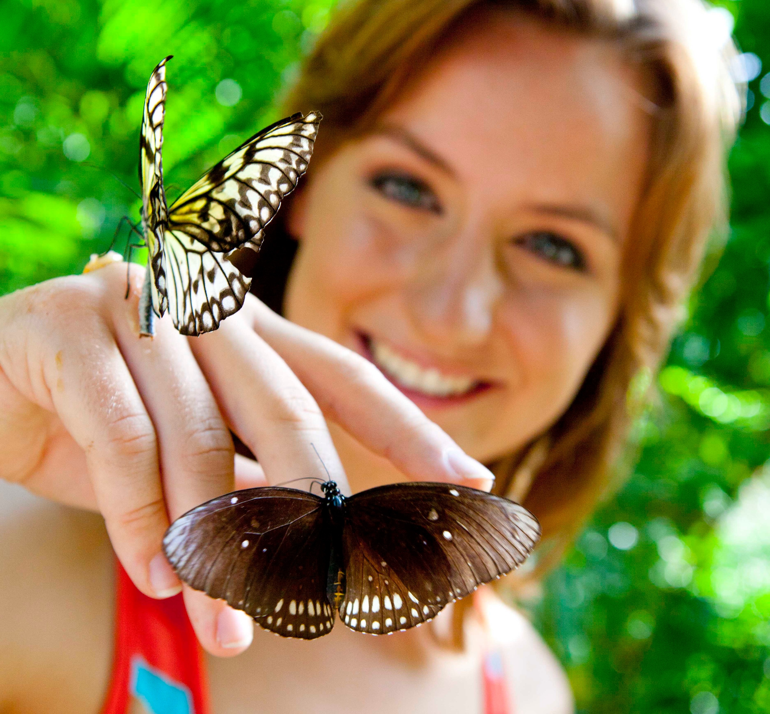 Woman smiling with two butterflies perched on her hand.