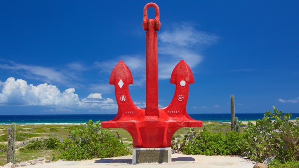 Large red anchor sculpture near beach with blue sky.