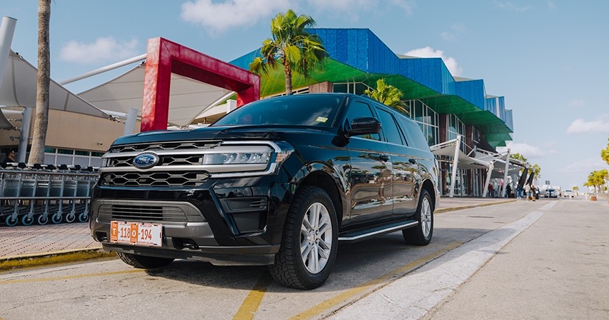 Black SUV parked by modern building with palm trees.