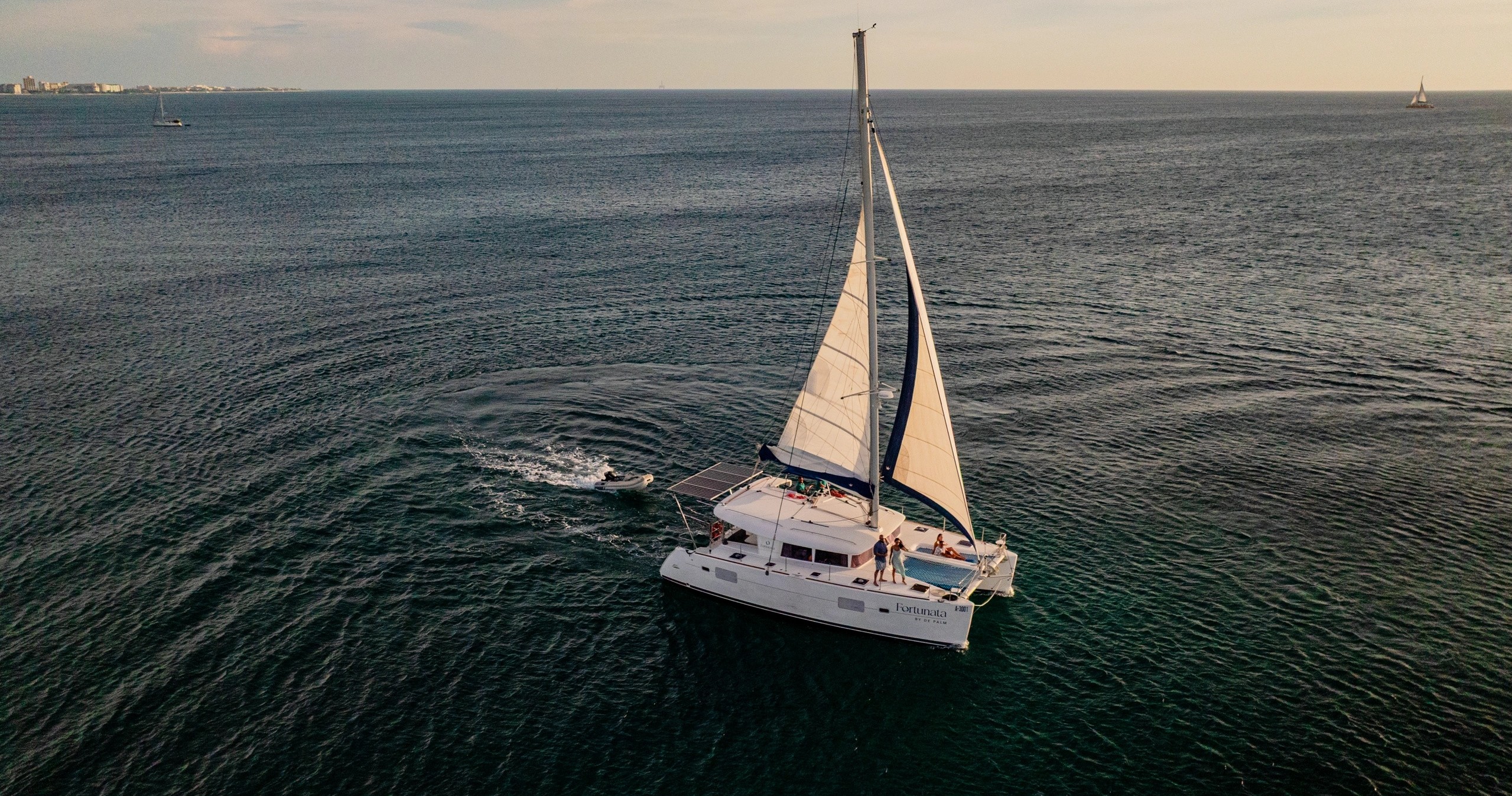 Sailboat with white sails on calm sea during sunset.