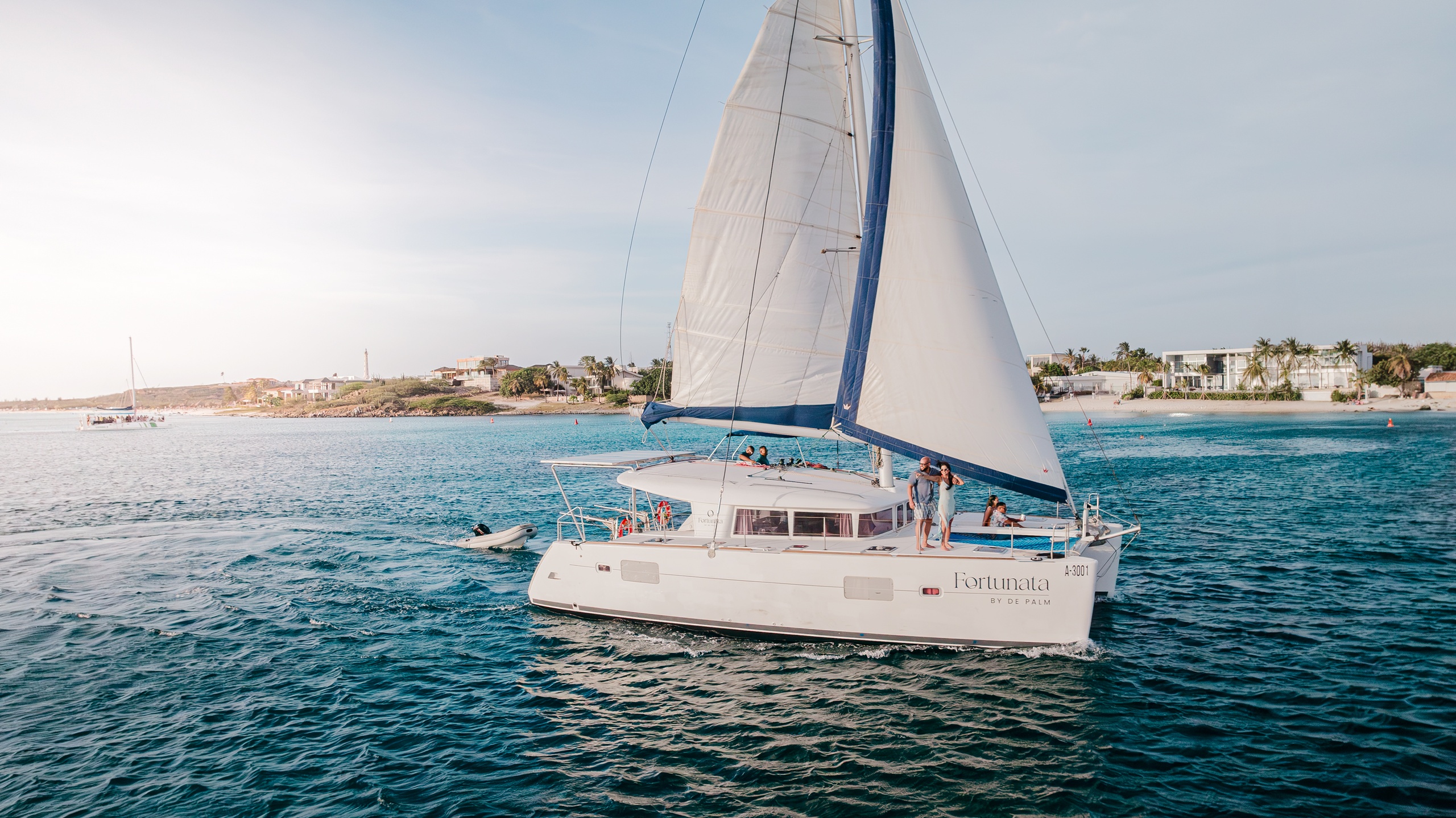 Sailboat on calm water near a shoreline with buildings and greenery.